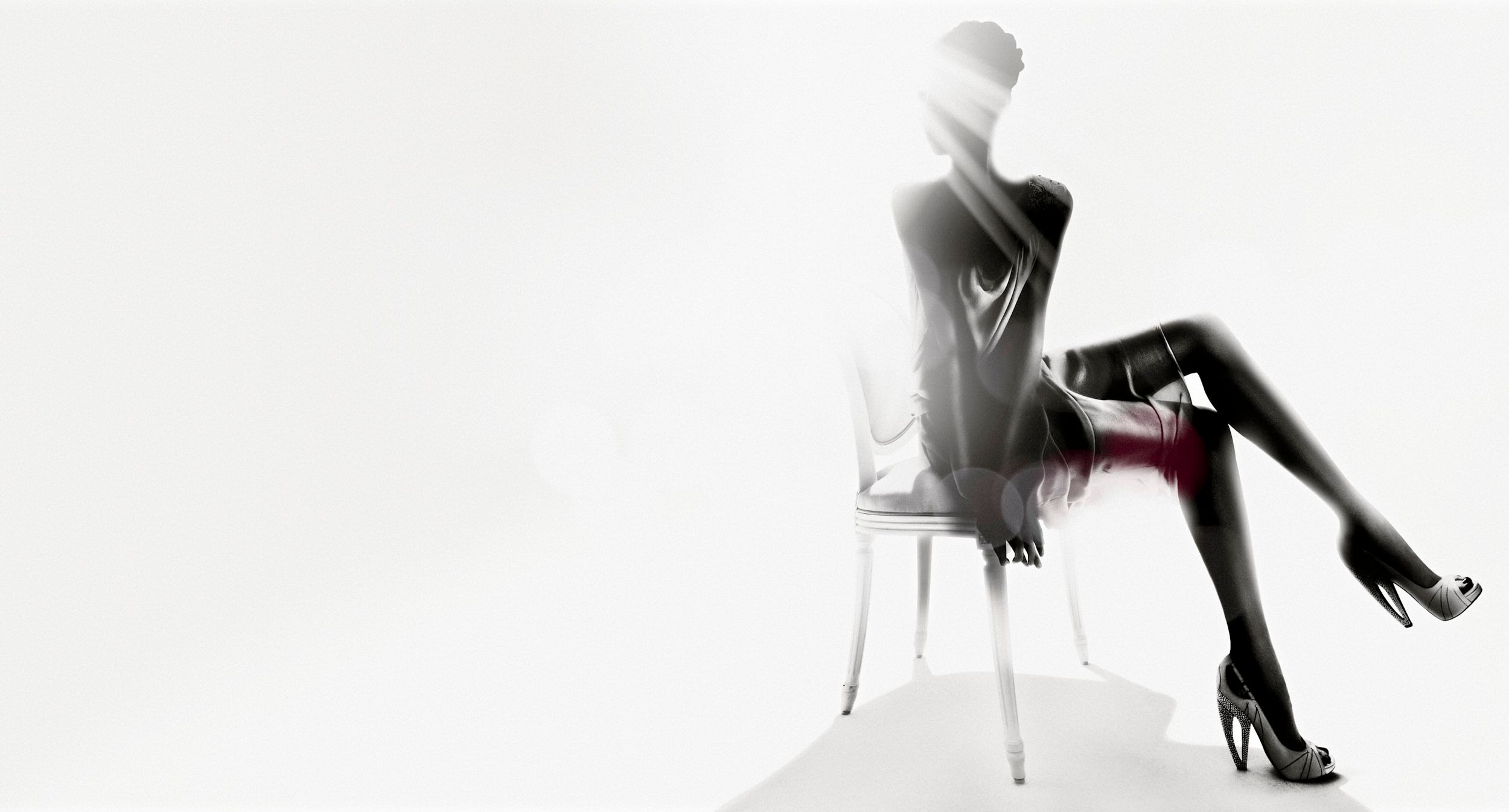 Elegant mannequin seated on a clear chair in a high-fashion pose wearing black stockings and heels.