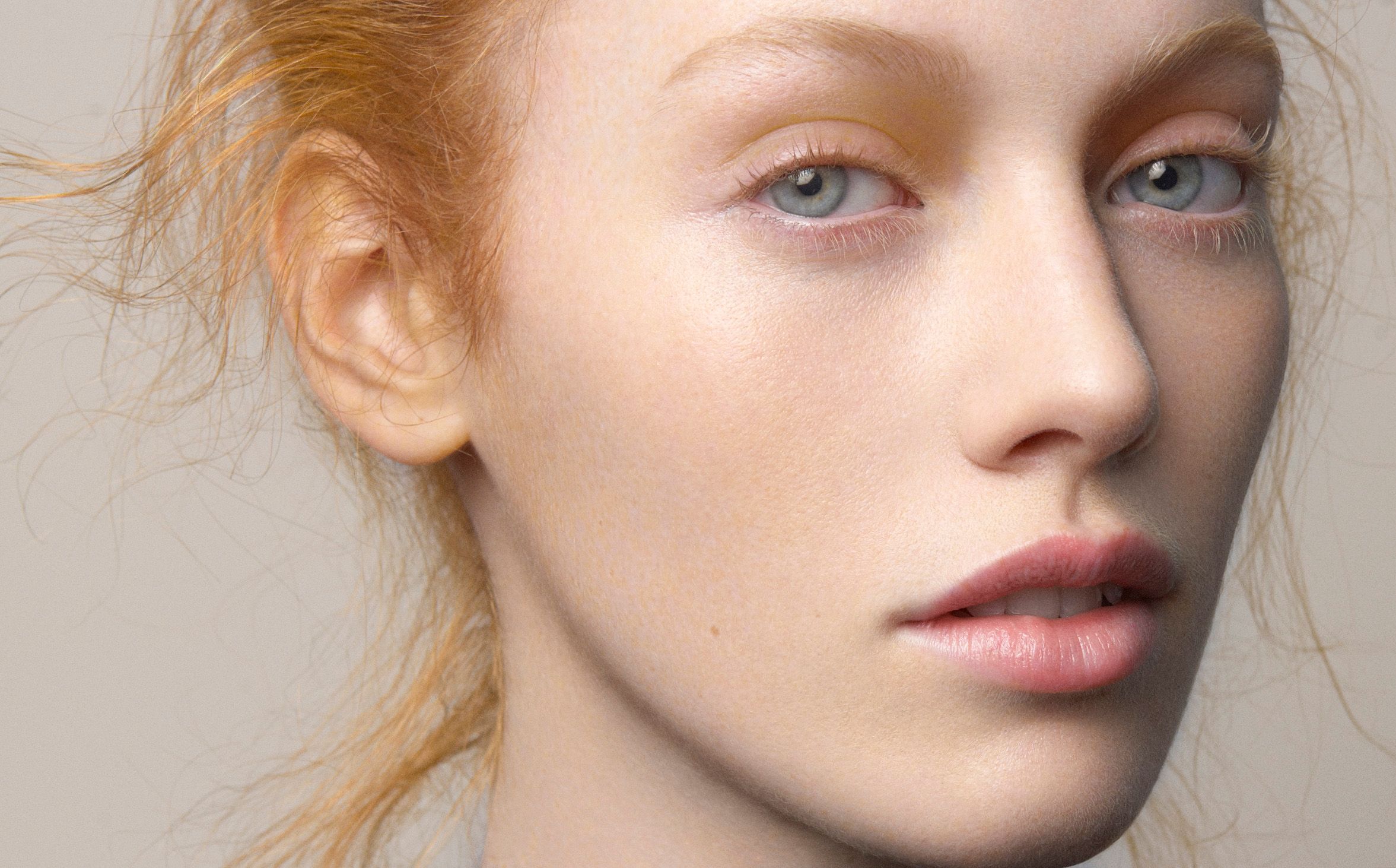 Close-up portrait of a young woman with red hair, freckles, and blue eyes against a light gray background.