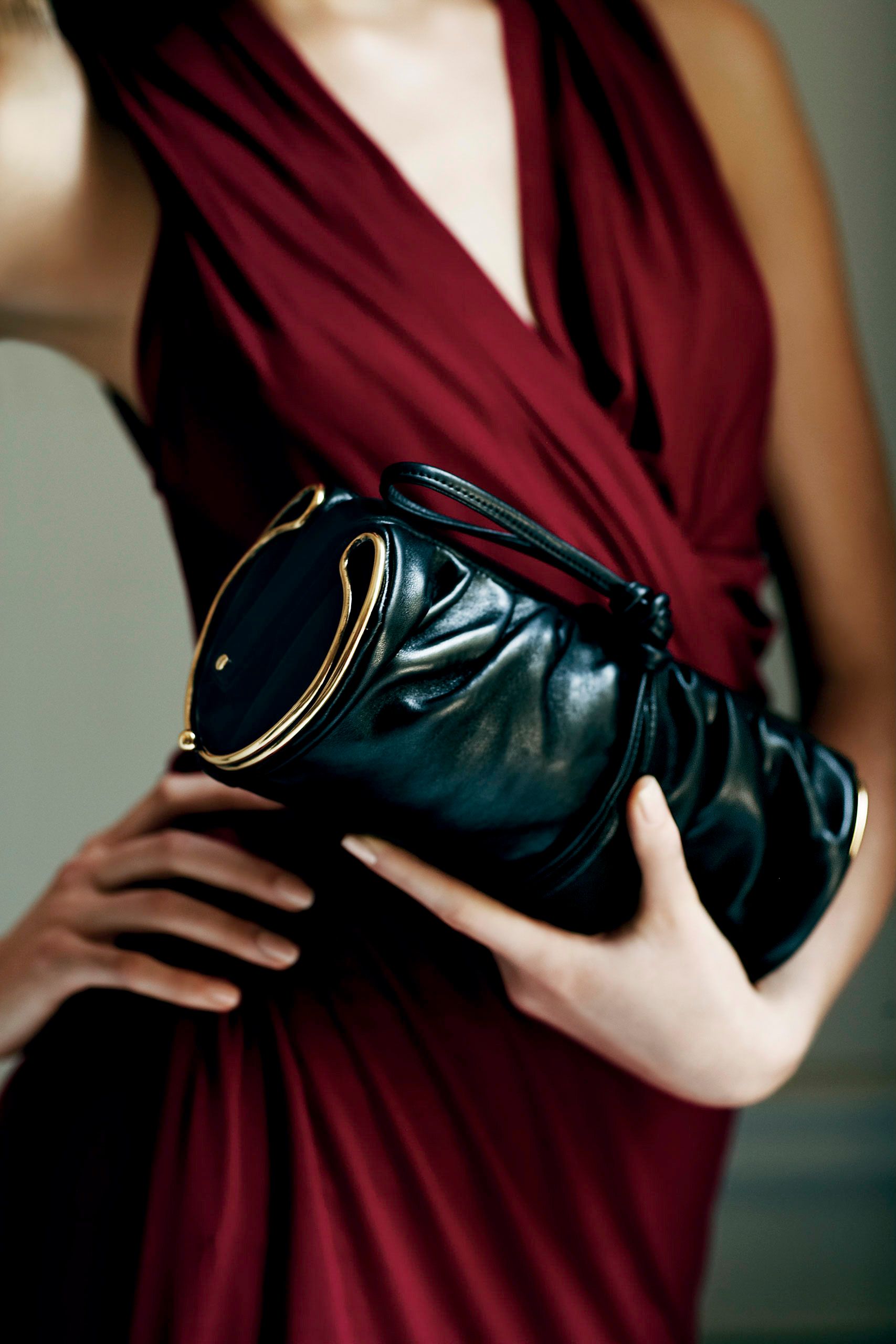 Woman in red dress holding black leather clutch bag with gold hardware accents.