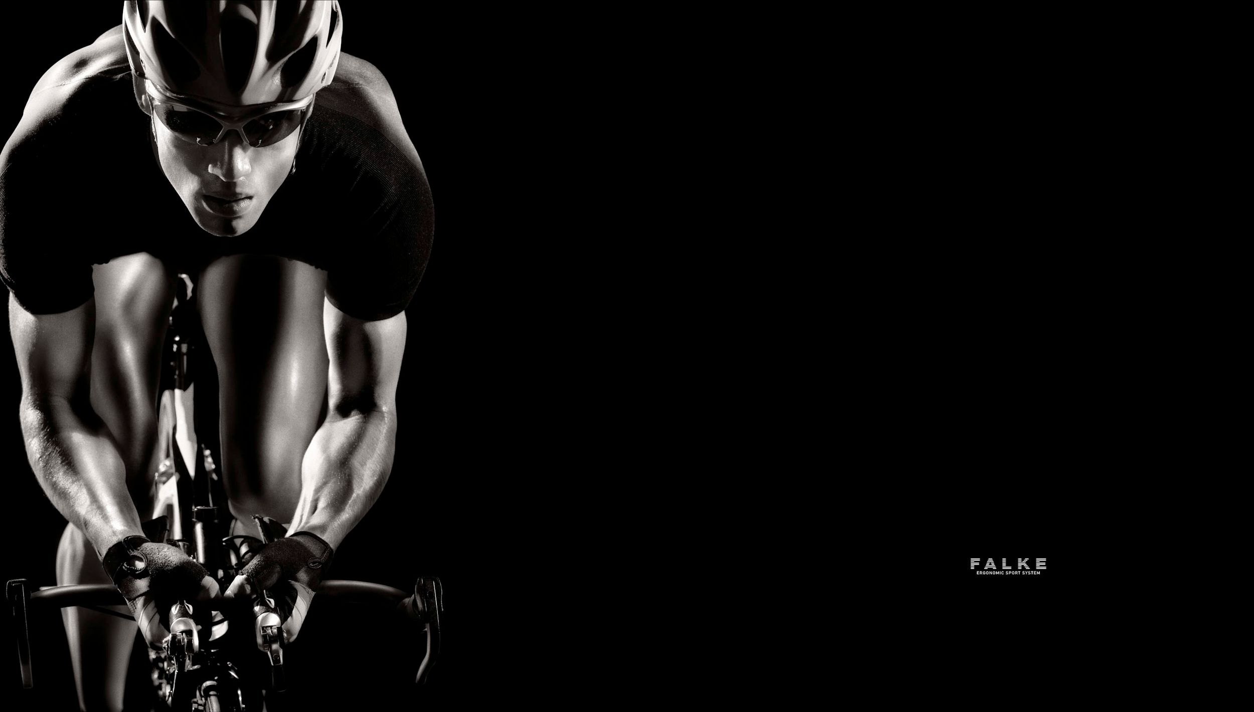 Muscular cyclist in black and white racing on a road bike, wearing a helmet, against a dark background.
