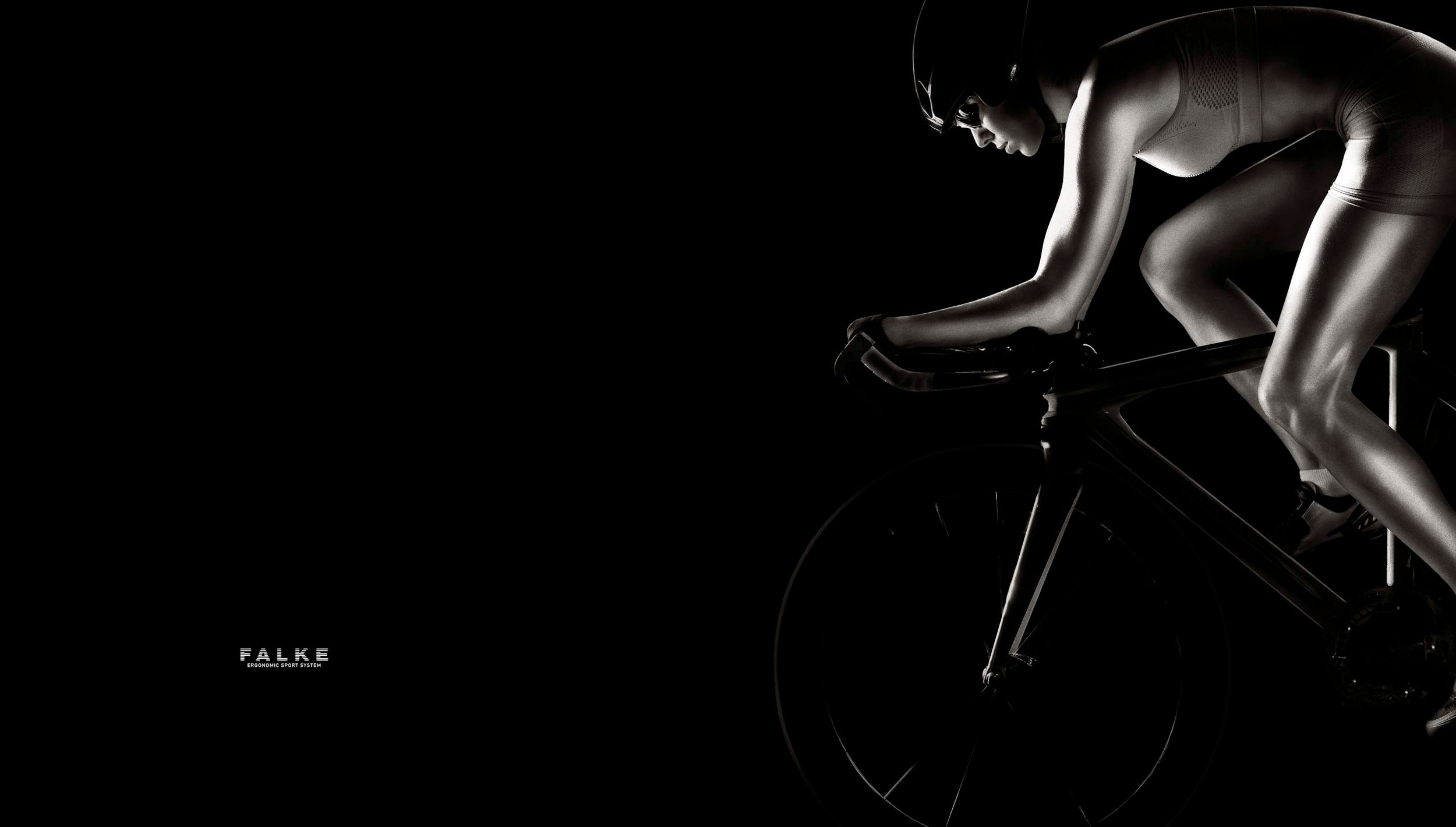 A cyclist in aerodynamic position rides a racing bike, dramatically lit against a stark black background.