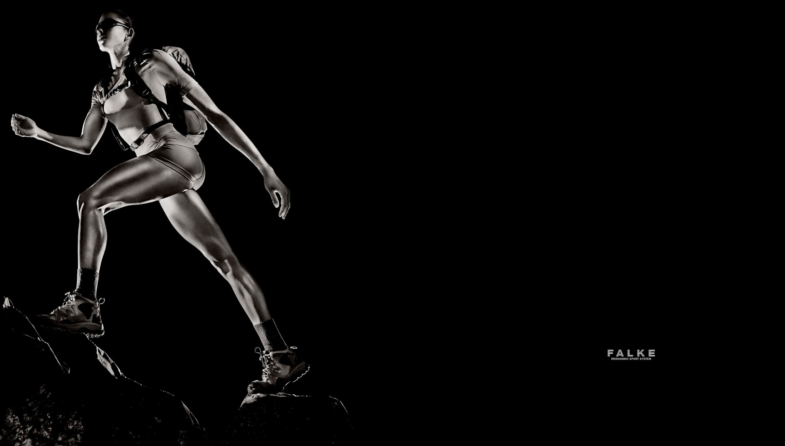Athletic woman running dynamically in sportswear against a dark background in a Falke ad.