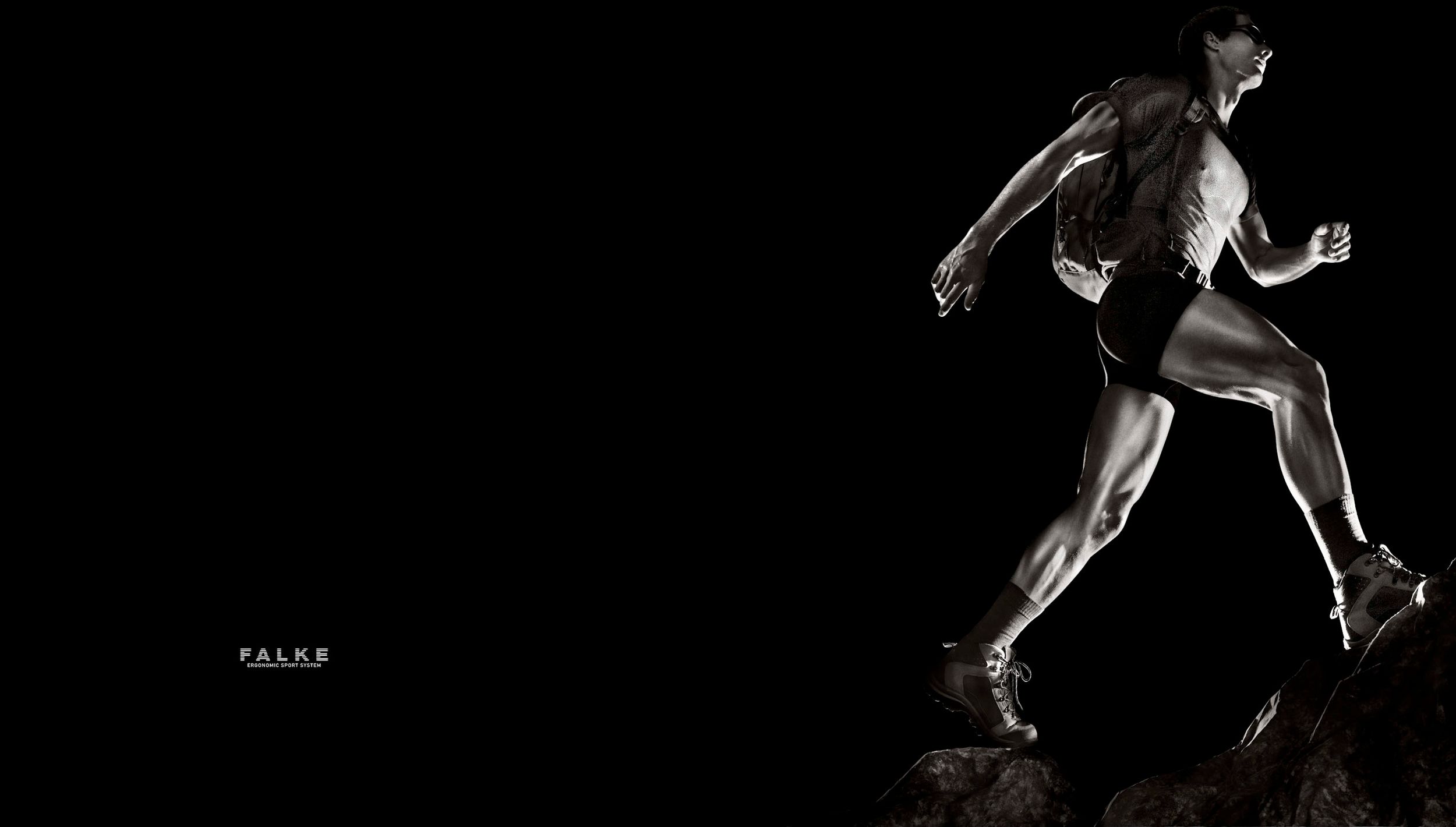 Muscular male athlete running dynamically on rocks against a dramatic black background in high contrast monochrome.