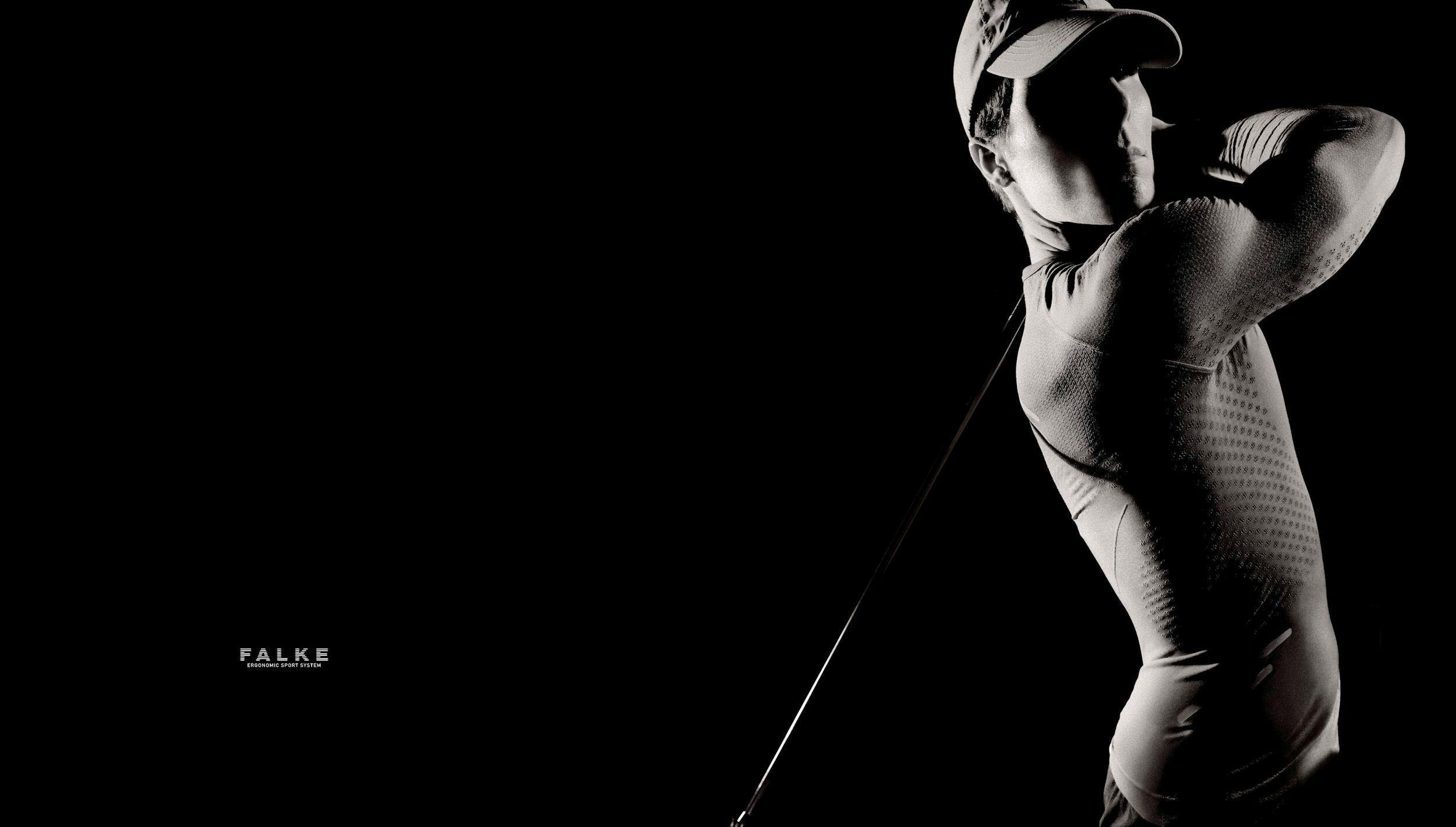 Black and white photo of a golfer mid-swing, wearing a cap and fitted outfit, dramatically lit against a dark background.