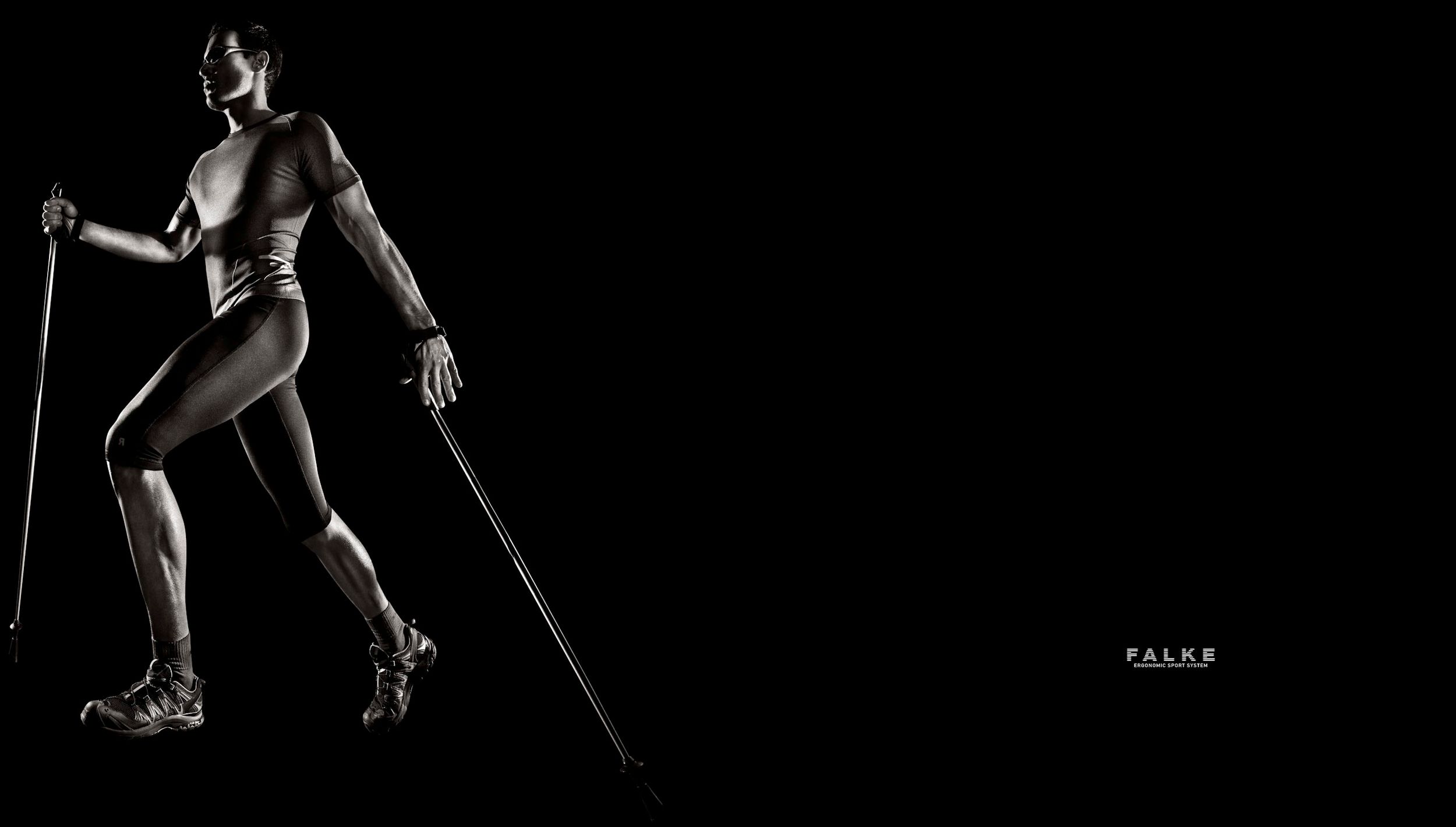 Athletic person in dark sportswear using Nordic walking poles in a dramatic black background studio shot.