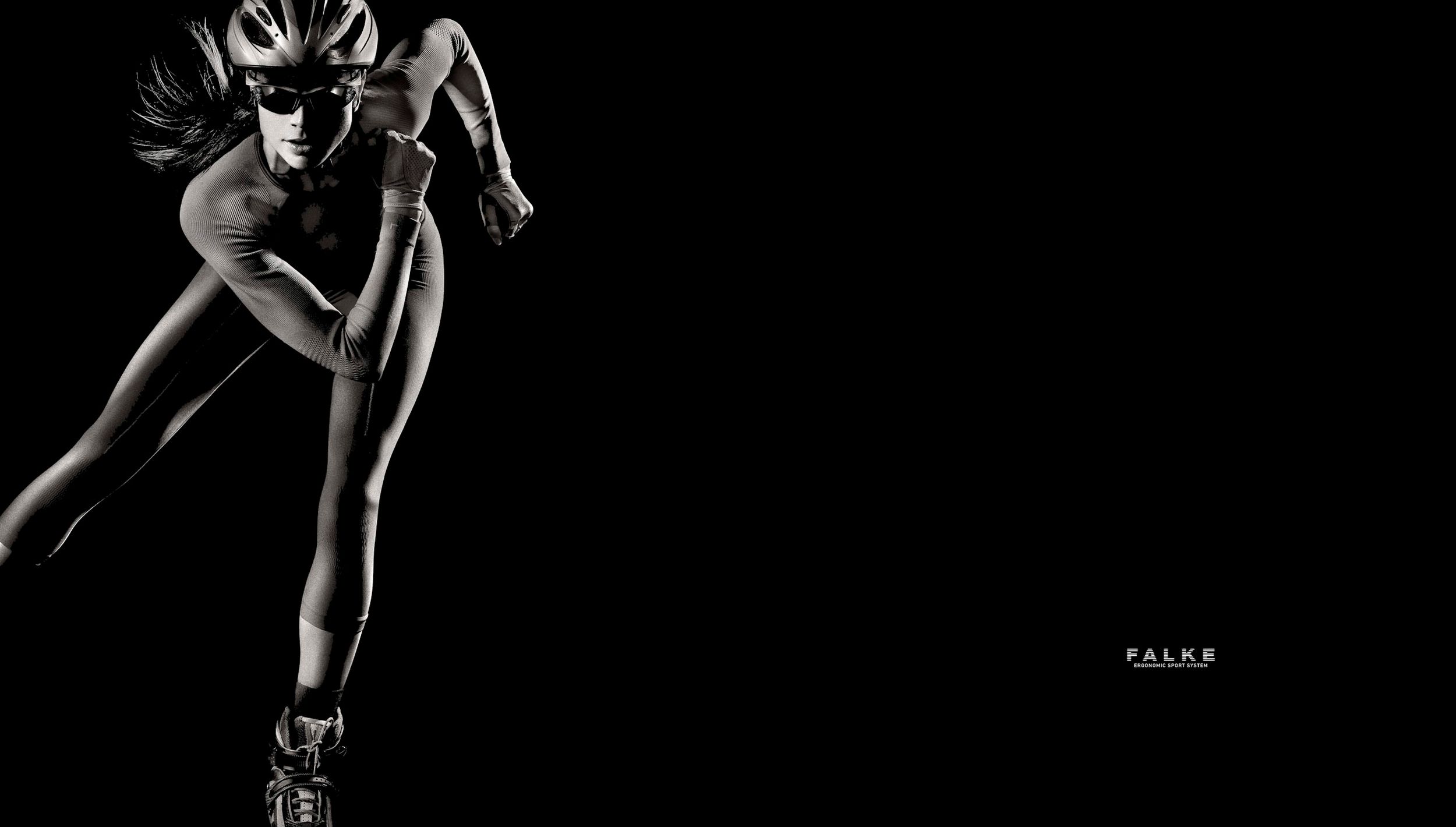 A dynamic athlete in cycling gear sprints powerfully against a stark black background in a dramatic monochrome photo.