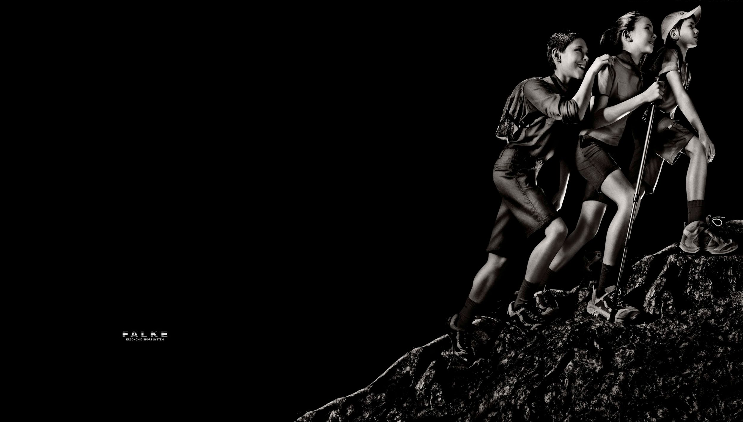 Black and white photo of three athletes climbing rocky terrain, wearing Falke sportswear, in a dramatic dark setting.