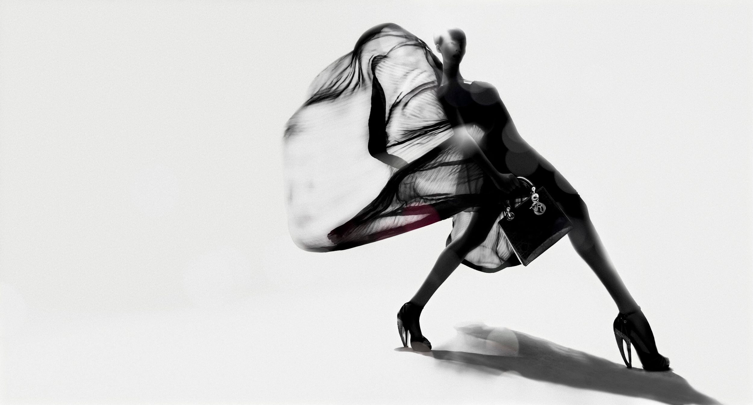 A dancer in black heels and skirt with flowing sheer fabric captured in dynamic motion against white background.