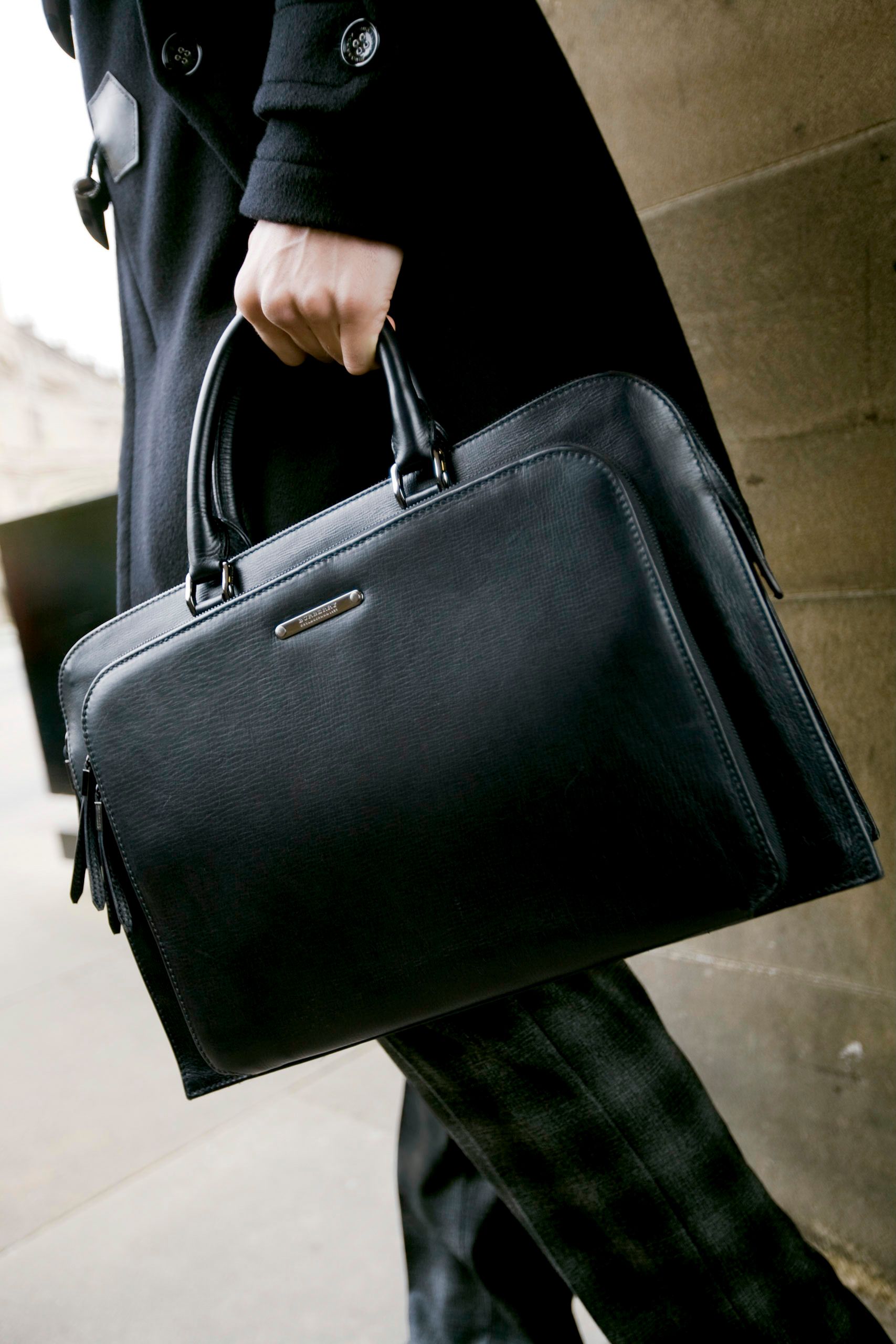 Man in black coat holding a sleek black leather briefcase, perfect for professional business use.