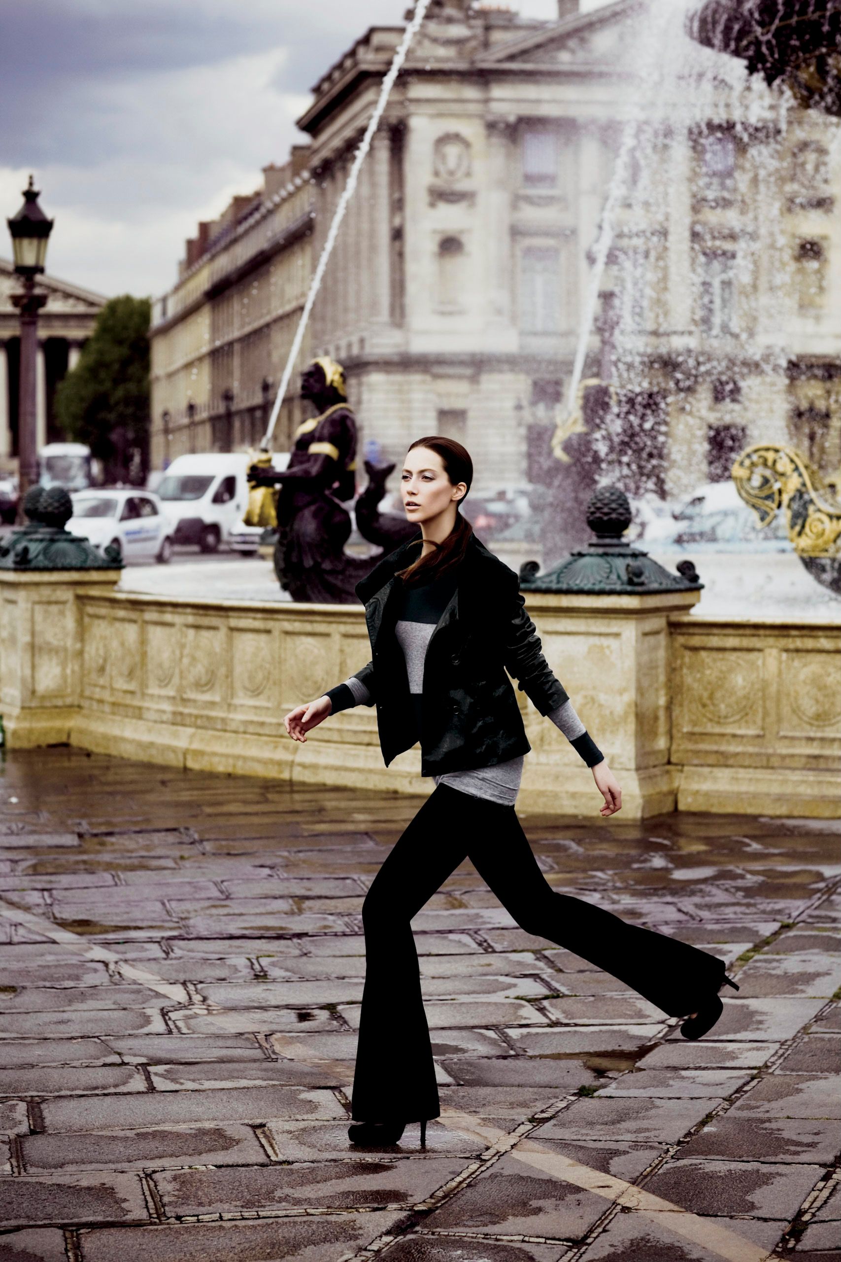 A stylish woman in black flare pants and jacket walks near a fountain at Place de la Concorde, Paris.