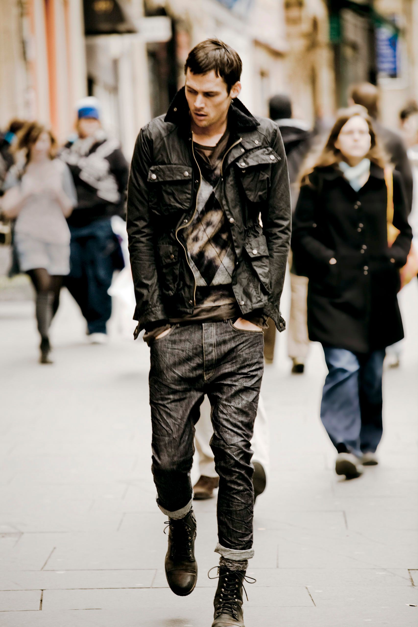 Stylish young man in black leather jacket, dark jeans, and combat boots walking on a busy urban street.
