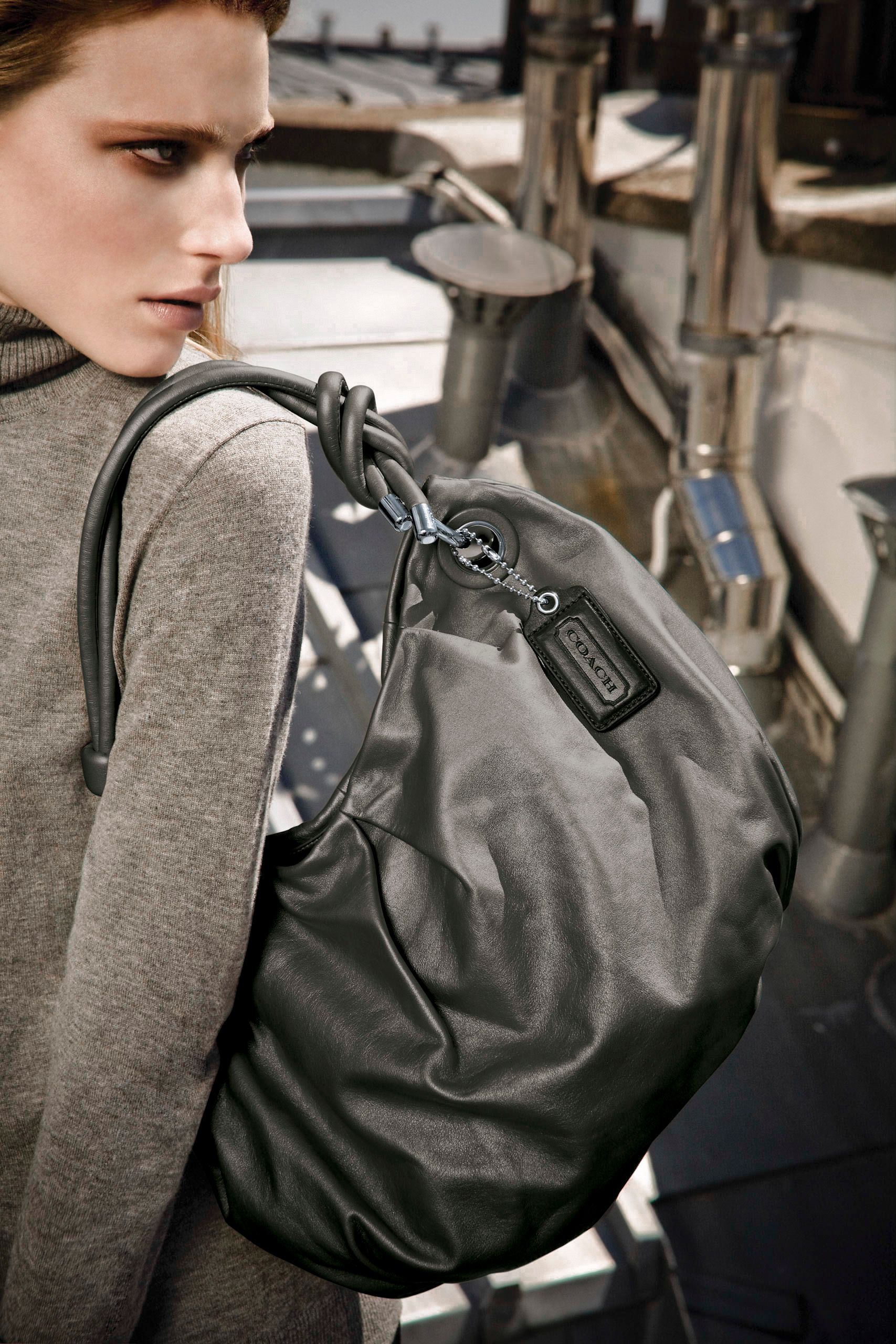 Woman carrying a large gray Coach drawstring bag over her shoulder in an urban setting.