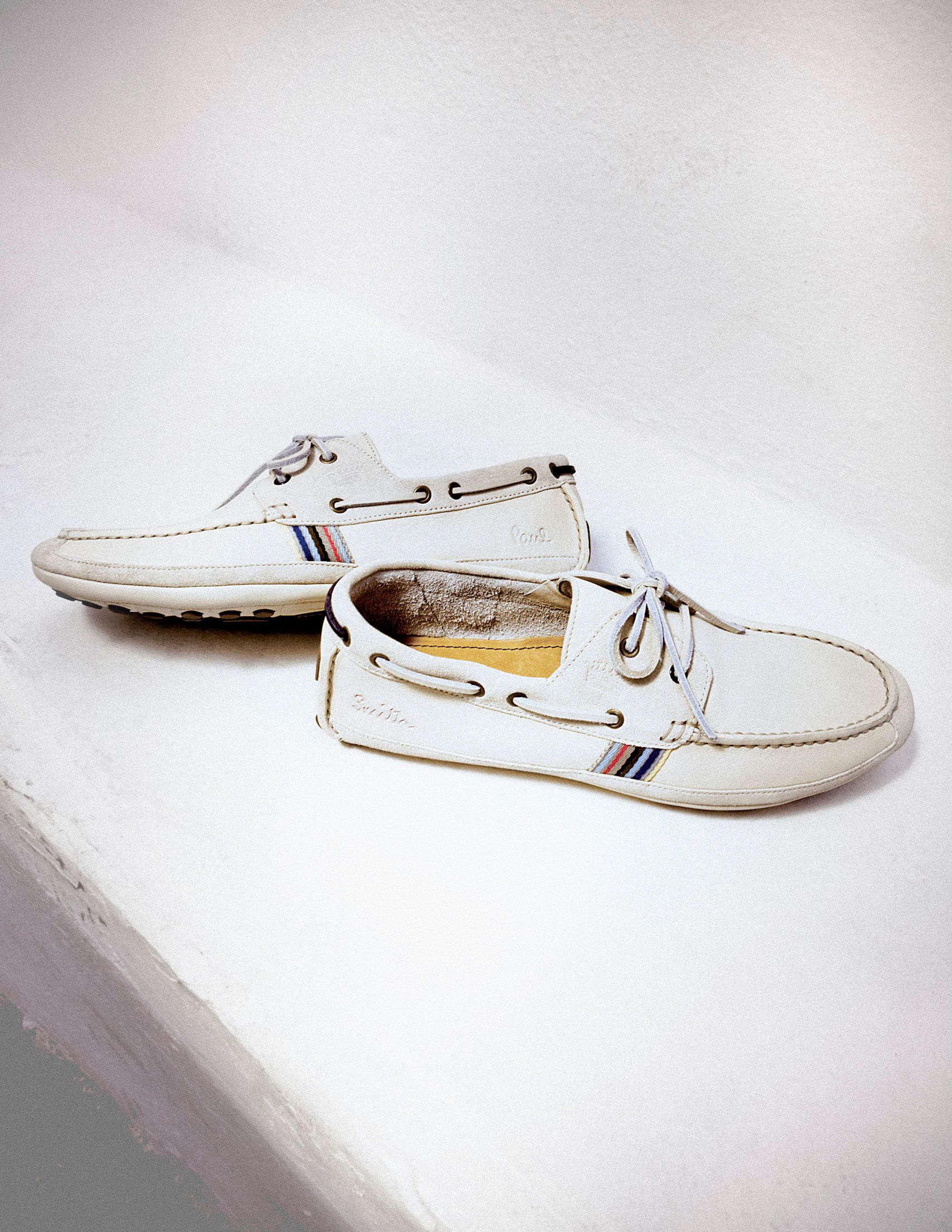White leather boat shoes with multicolor stripe detail and lace-up front, displayed on a white surface.