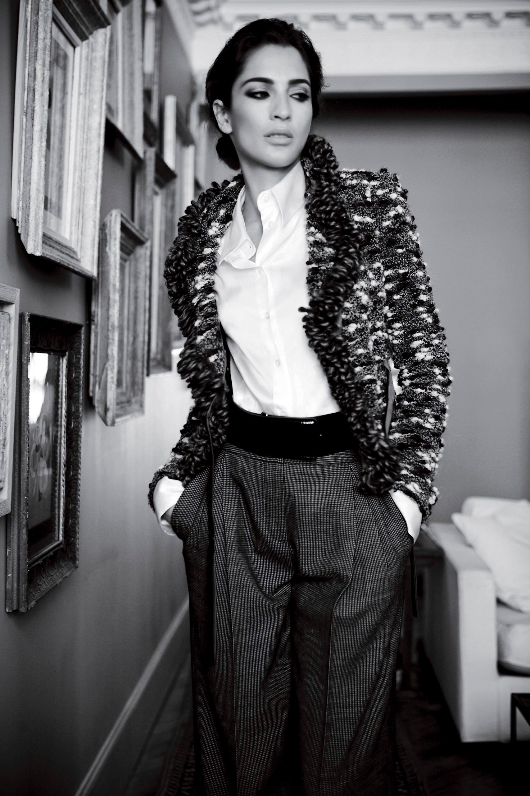 Woman in textured blazer, white shirt, and wide-leg trousers poses elegantly in black and white photo.