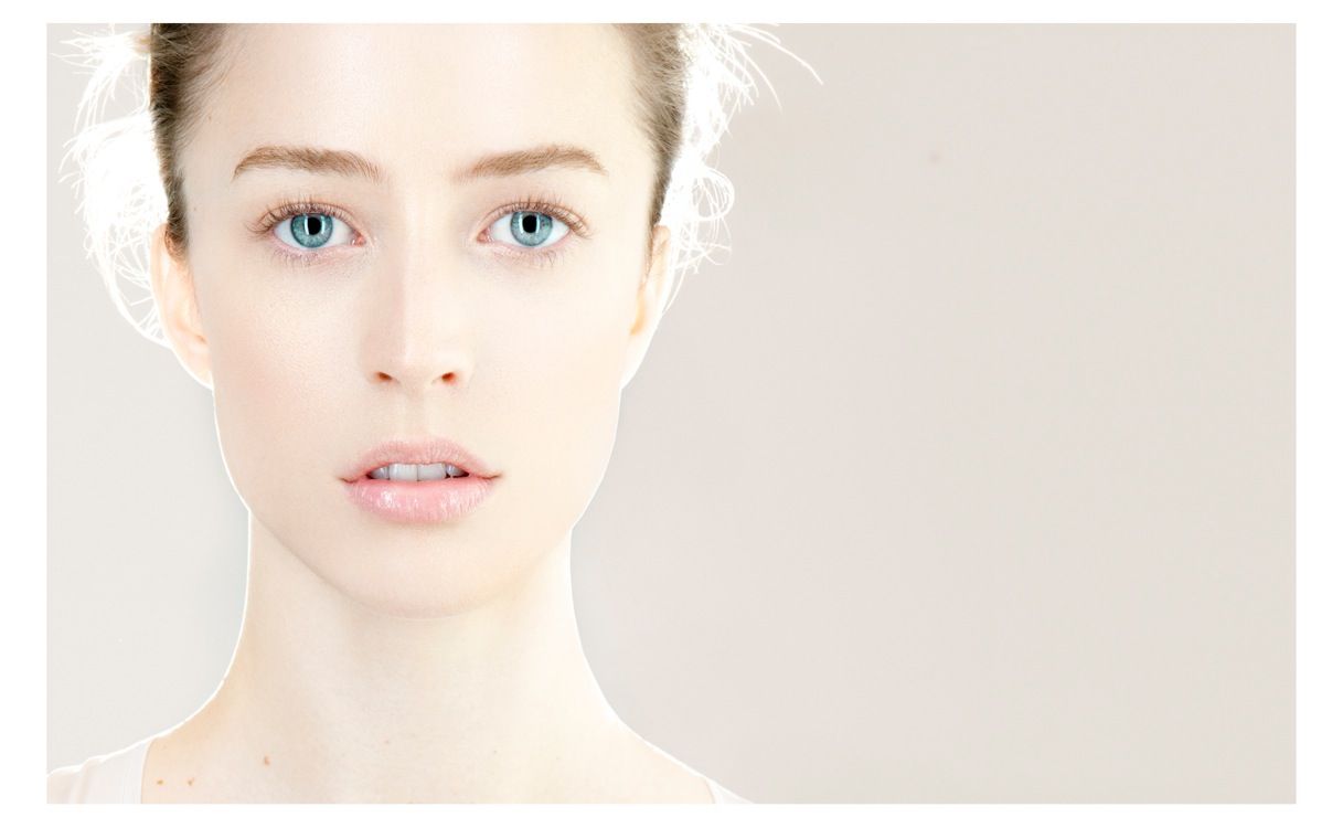 Close-up portrait of a young woman with blue eyes and fair skin against a light background.