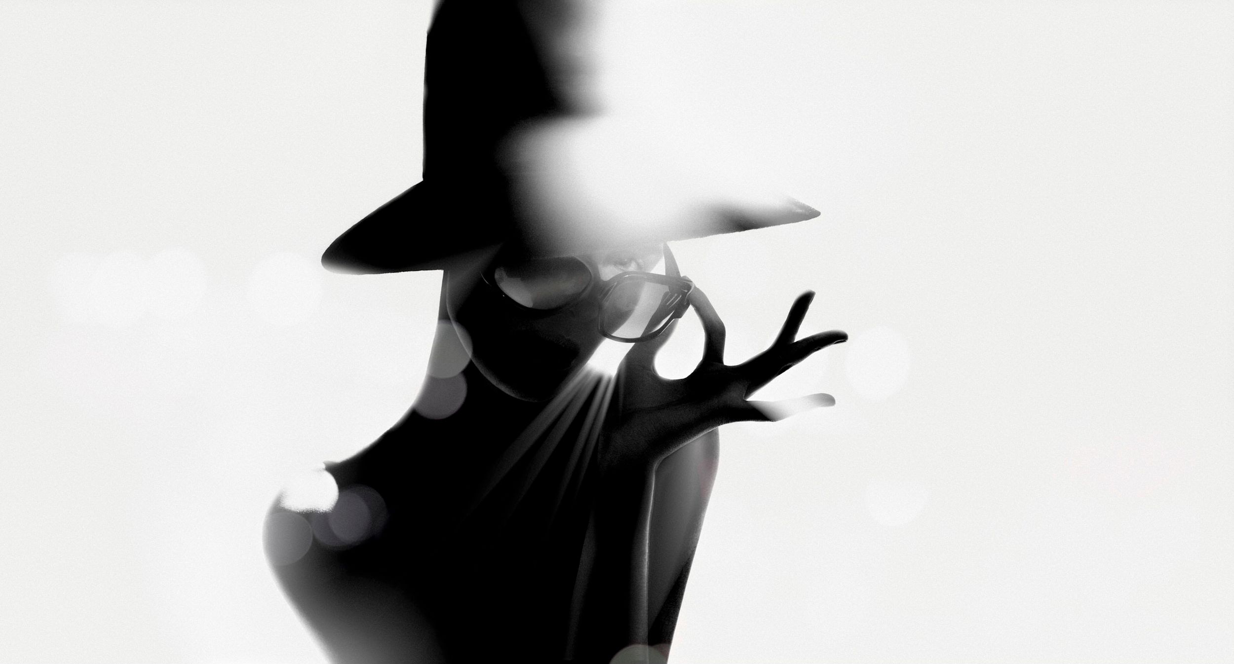 Silhouette of a person wearing a wide-brim hat with an outstretched hand in a dramatic black and white photo.