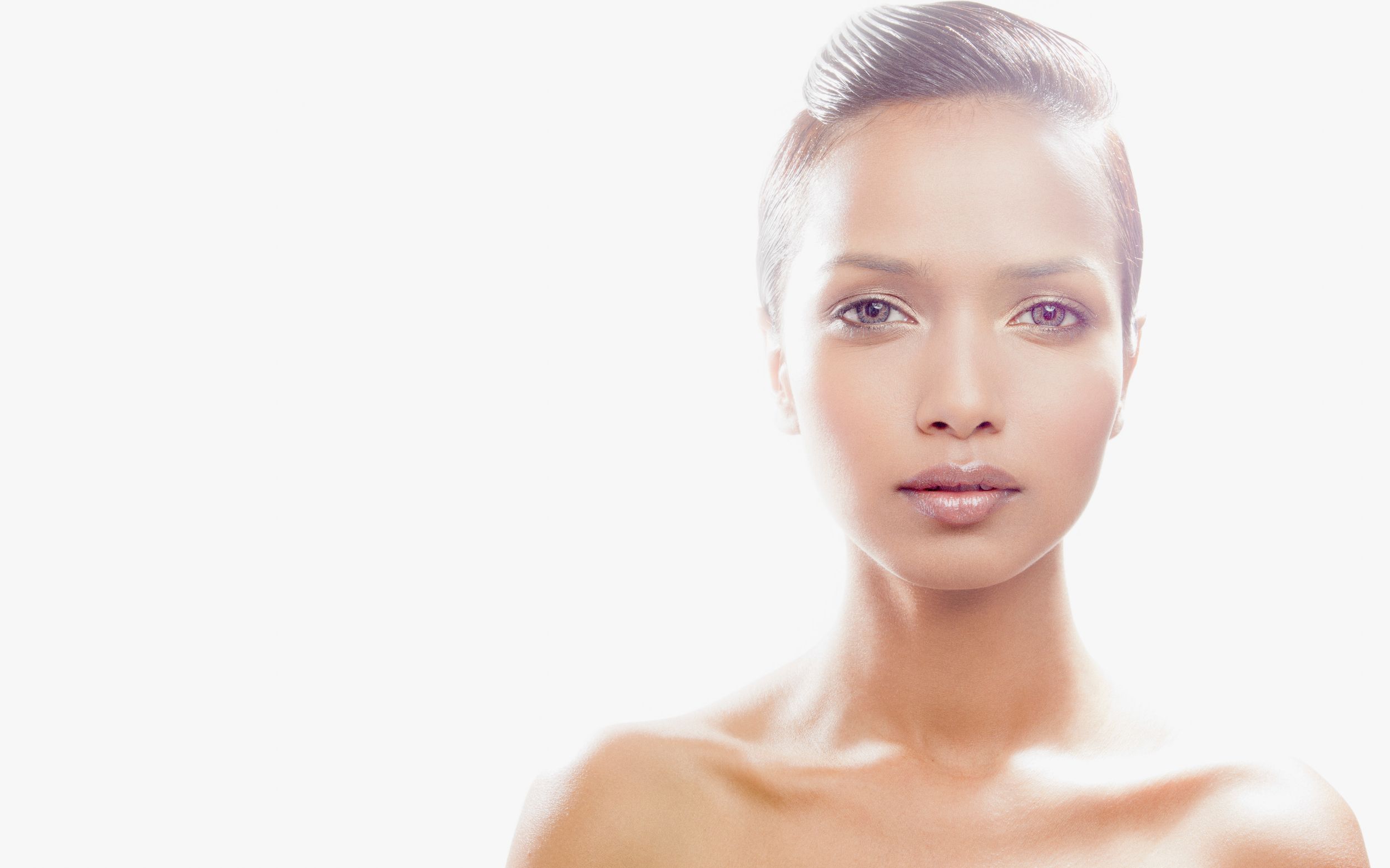 Close-up portrait of a young woman with flawless skin and sleek hair against a white background.