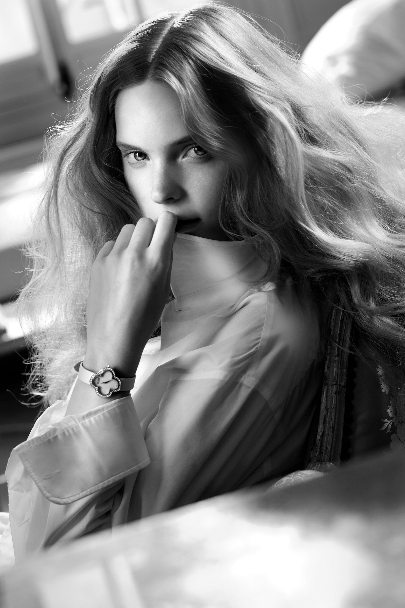 Black and white close-up of a young woman with flowing hair wearing a watch, gazing at the camera.