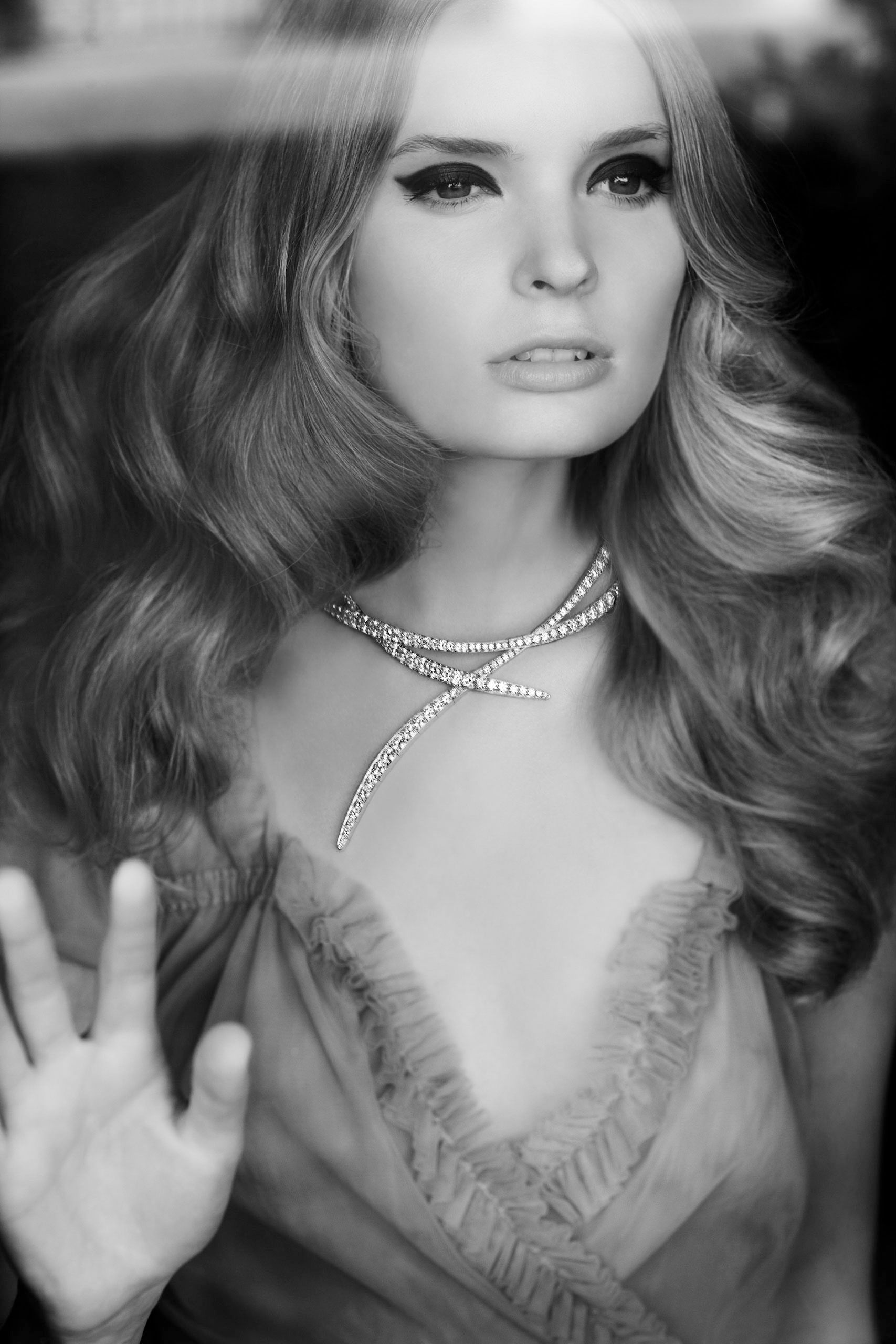 Black and white portrait of a woman with voluminous wavy hair wearing a diamond snake necklace and ruffled top.