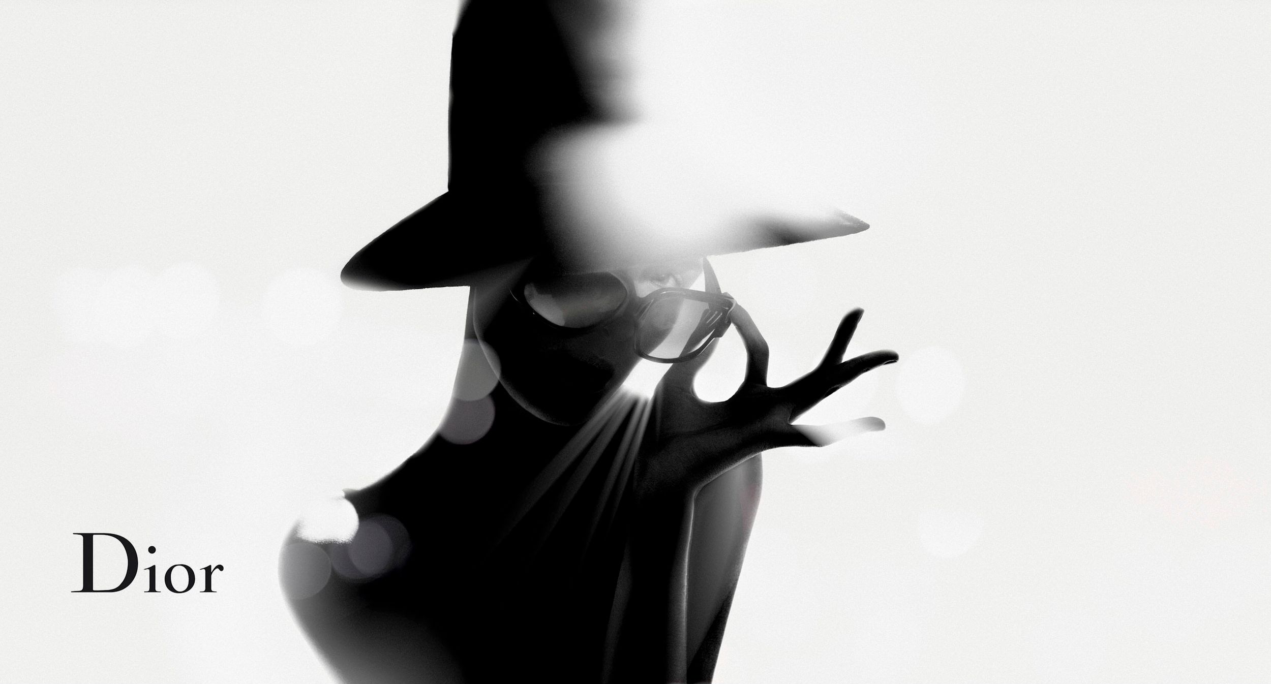 Dior fashion advertisement featuring a silhouetted figure in a black dress and wide-brim hat in artistic motion.