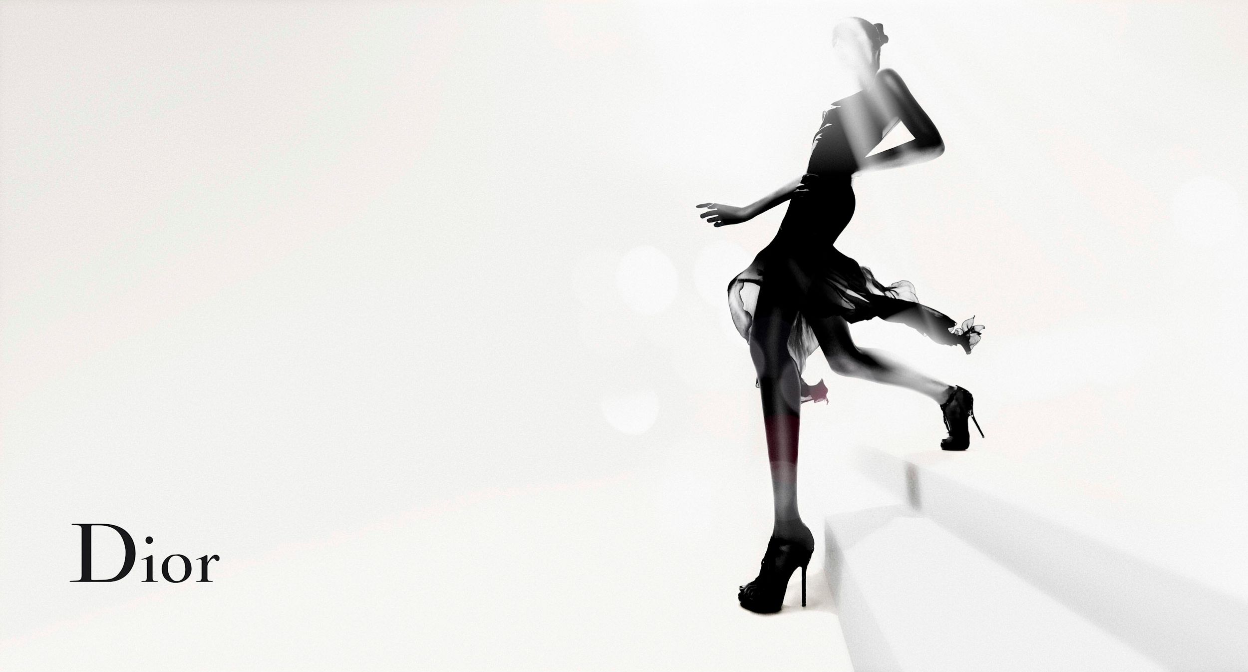 Dior fashion ad featuring a model in a black dress and heels striking a dynamic pose on a white background.