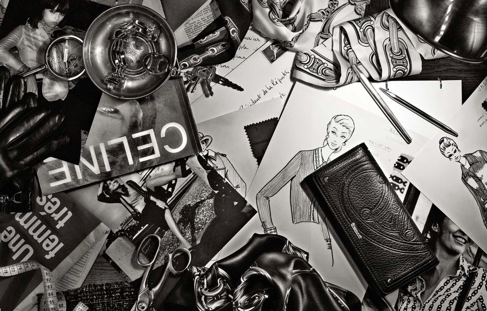Black and white flat lay of Celine fashion sketches, accessories, and brand materials arranged artistically.
