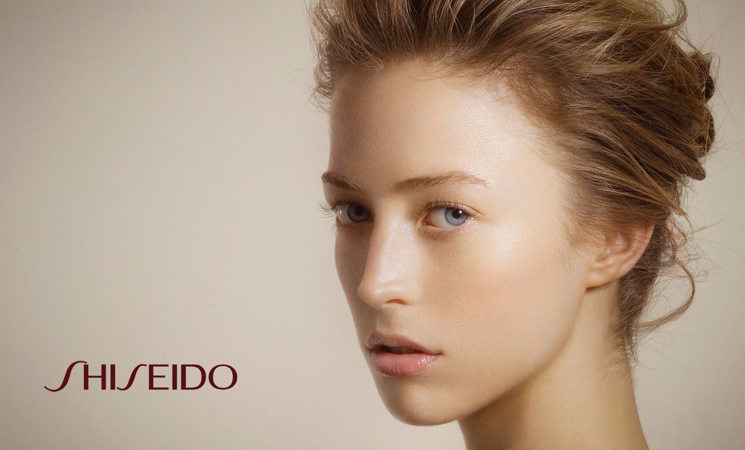 Young woman with elegant updo hairstyle and flawless skin poses for Shiseido beauty brand advertisement.
