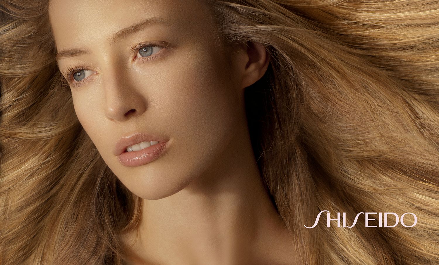 Shiseido beauty ad featuring a young woman with flowing blonde hair and flawless skin against a neutral background.