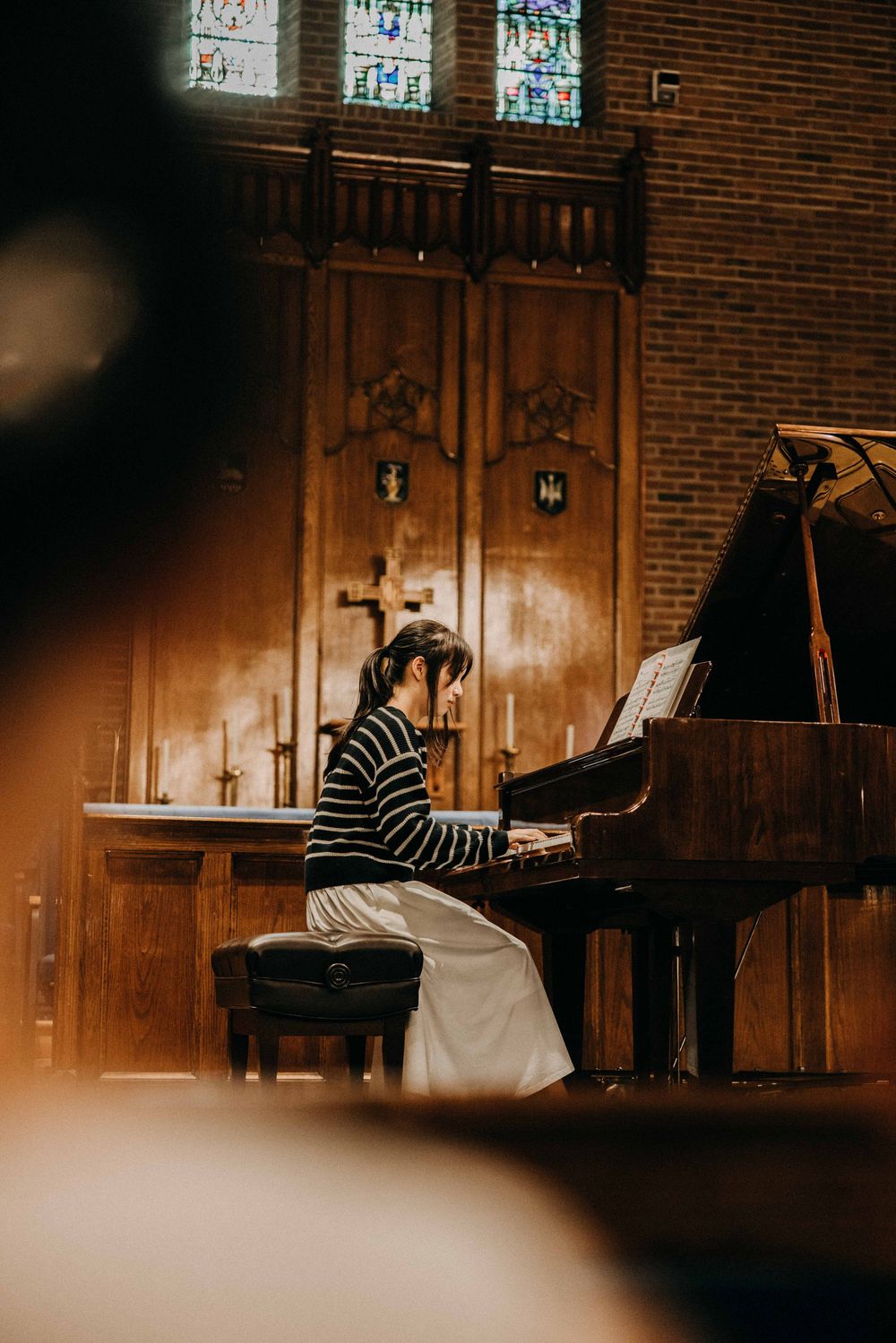 A pianist performs on a grand piano inside a warmly lit church with stained glass windows and wooden altar backdrop.