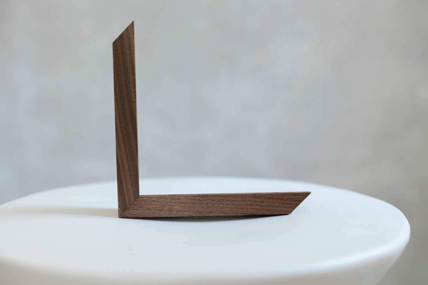 Dark walnut wood L-shaped bracket displayed upright on a white round table against a neutral gray background.