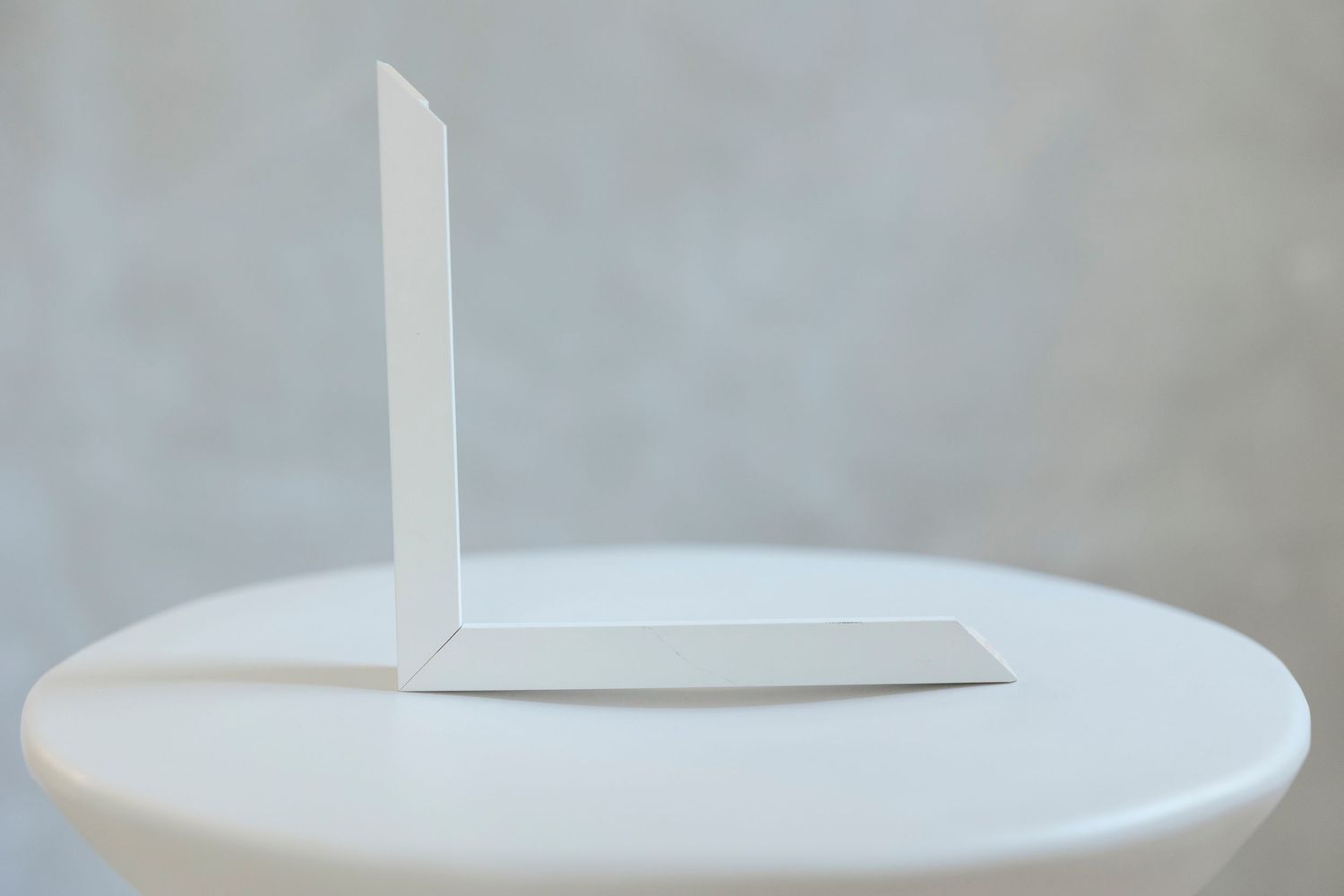A minimalist white paper bookend displayed on a round white table against a soft gray background.