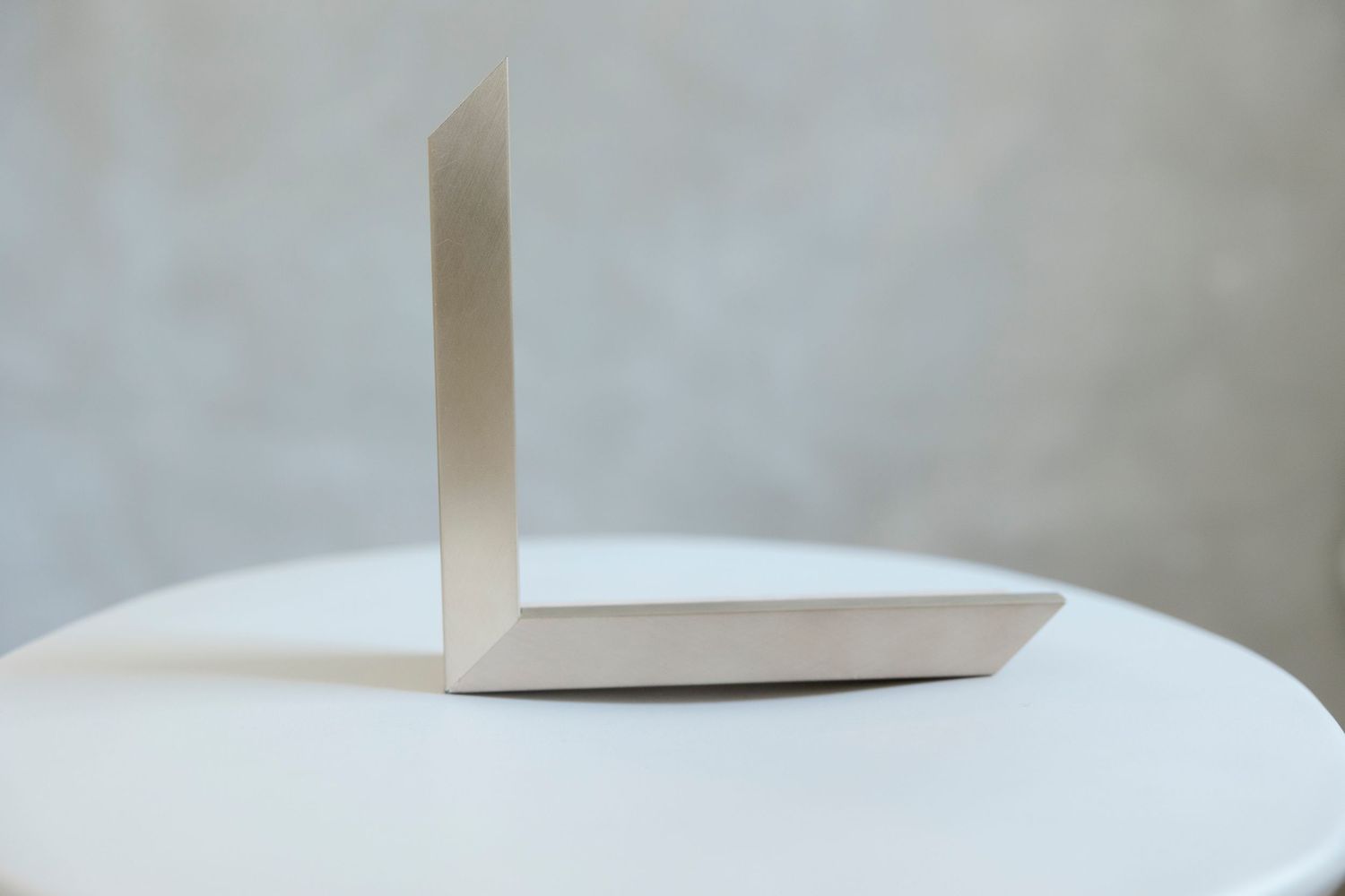 A minimalist beige paper or cardboard L-shaped bookend sitting on a white round table against a gray wall.