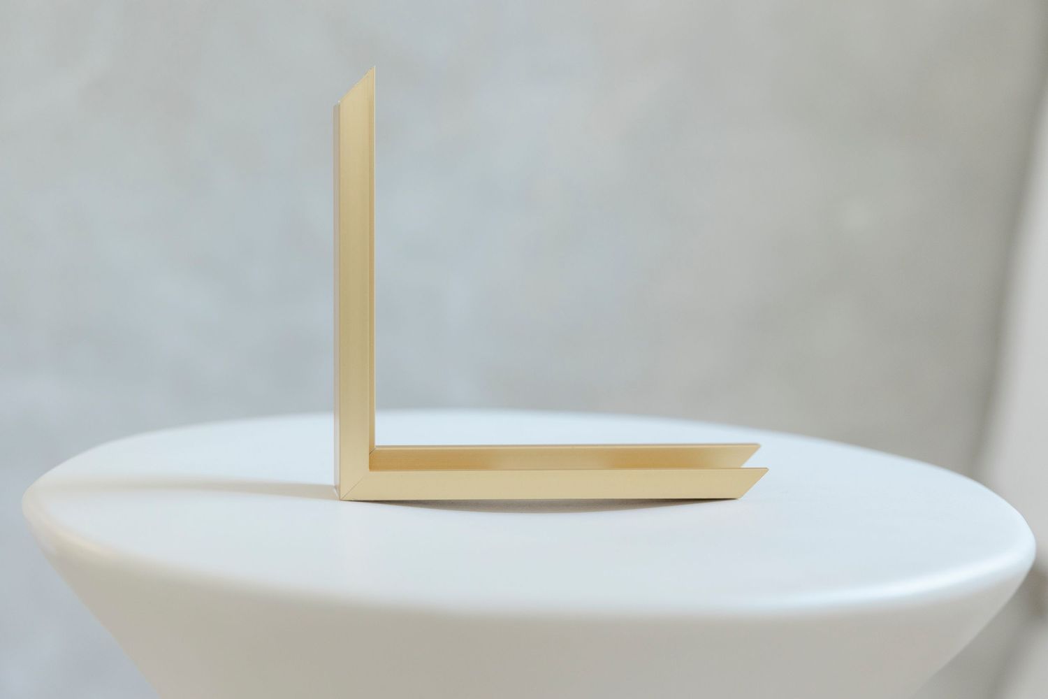 Gold metallic L-shaped bracket or bookend displayed on a white round pedestal against a neutral background.