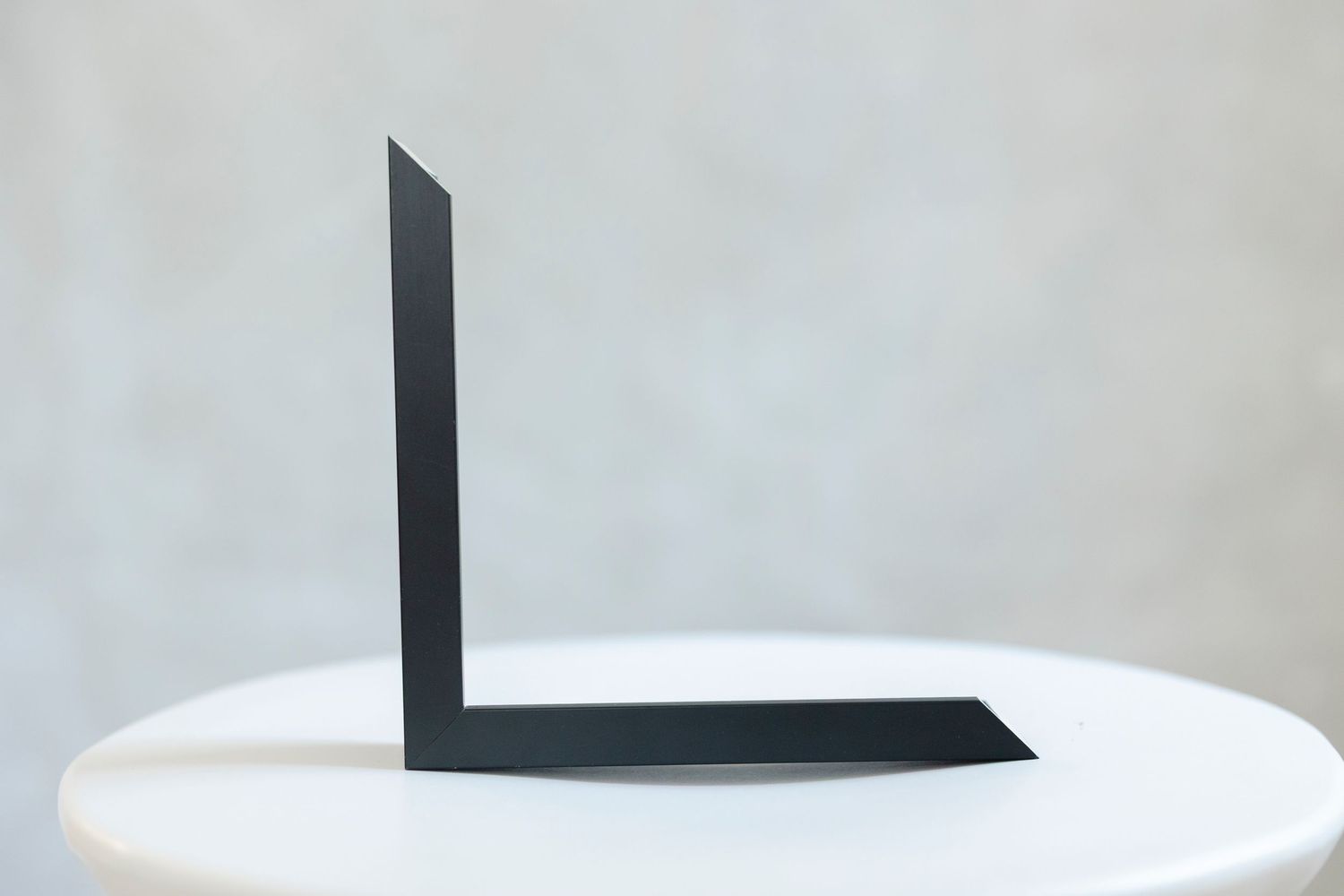 Black metal L-shaped bookend displayed on a white round table against a gray background.