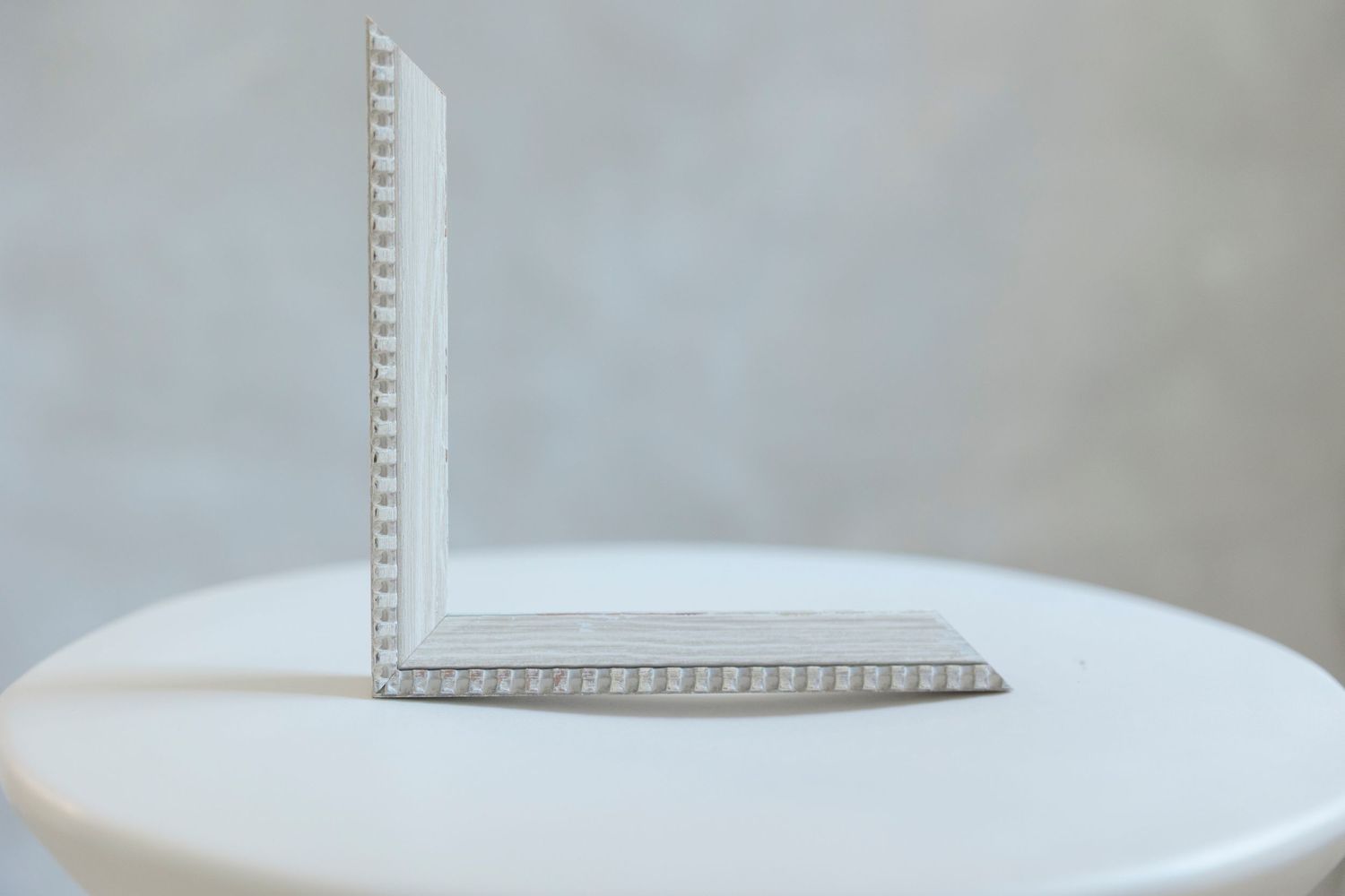 White L-shaped aluminum angle bracket with textured edges displayed upright on a white round table against gray background.