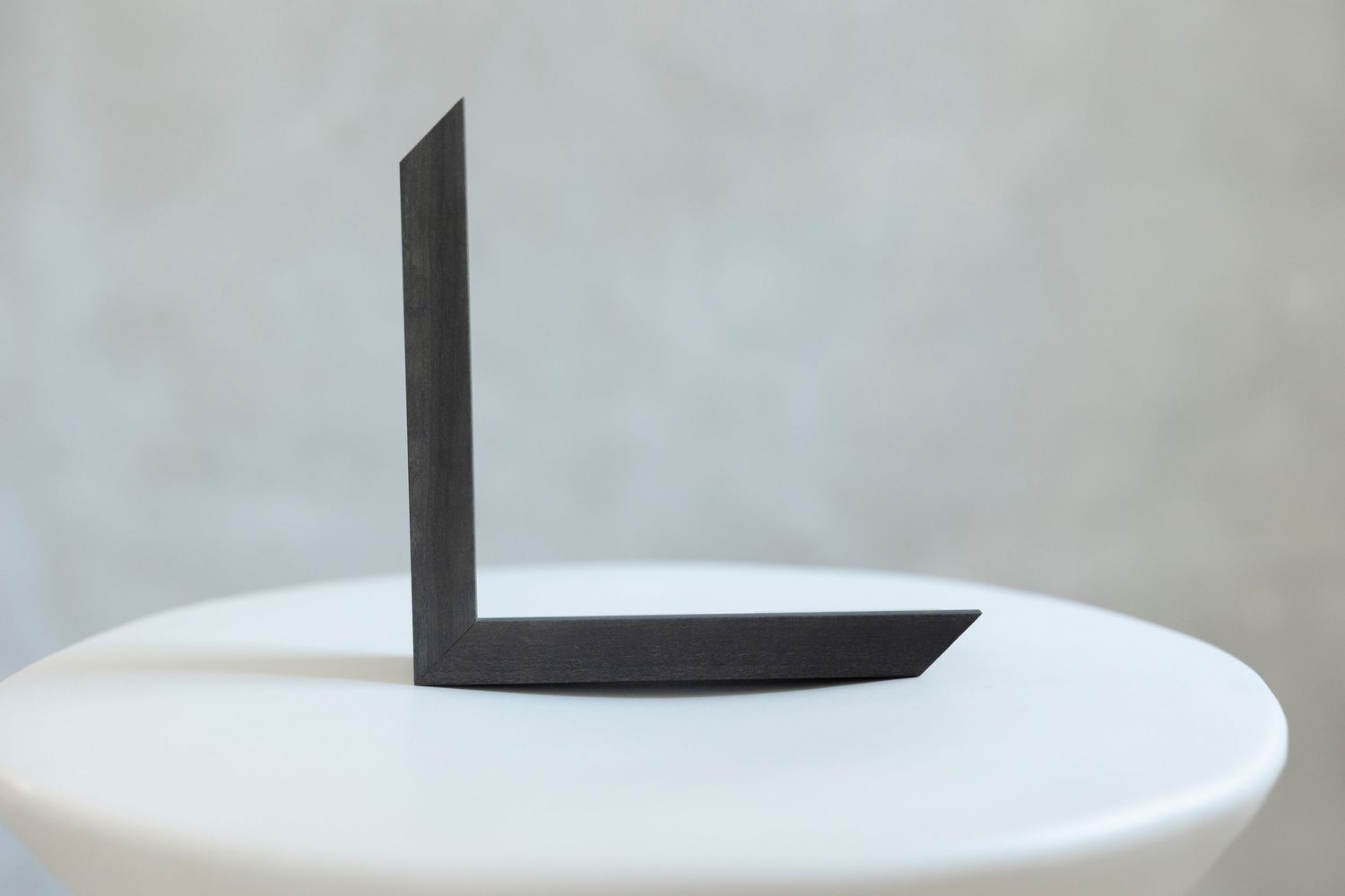 Minimalist dark metal bookend in an L-shape displayed on a white round table against a gray background.