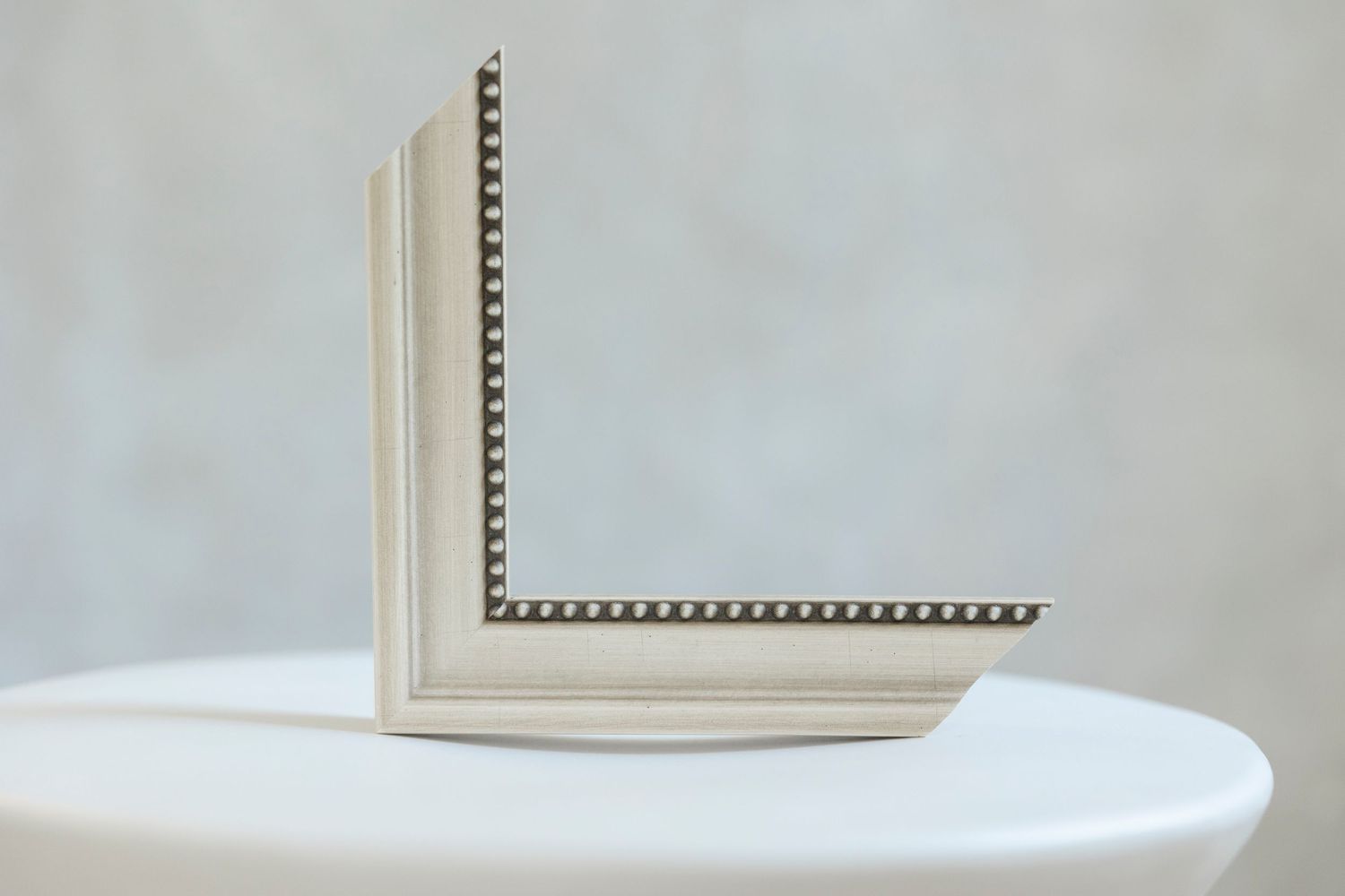 Elegant cream picture frame corner with decorative beaded detail displayed on a white pedestal against a gray background.