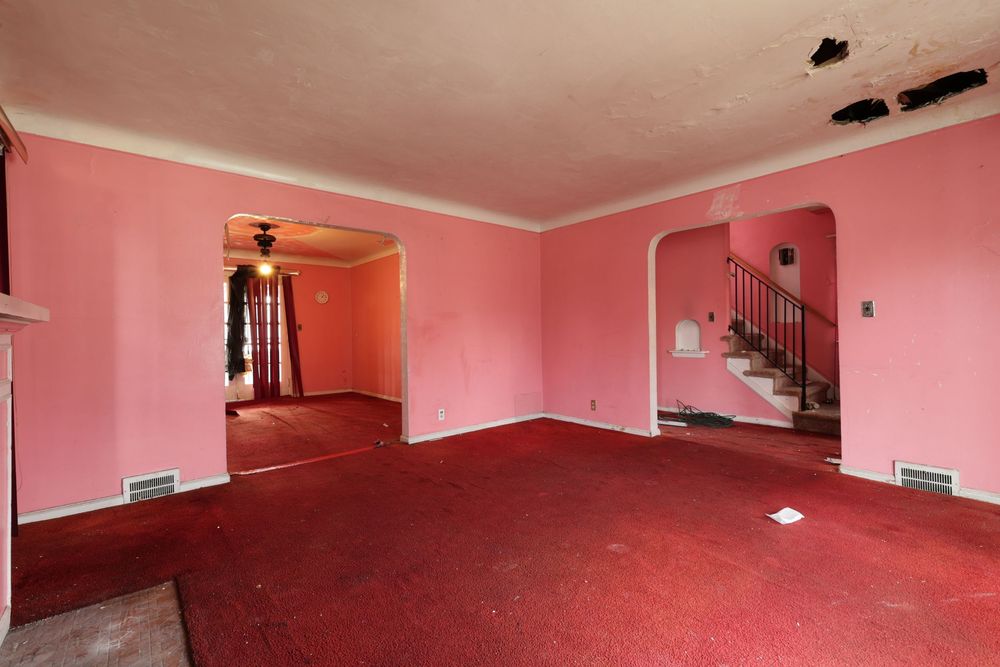 Empty living room with pink walls, red carpet, arched doorways, and a staircase in a vacant home. ceiling damageDetroit Michigan