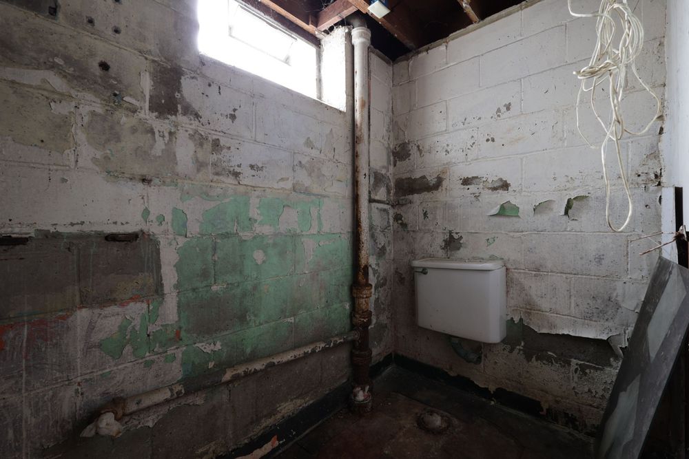 Abandoned derelict room with deteriorating concrete block walls, exposed pipe, loose wiring, and old radiator. Detroit Michigan