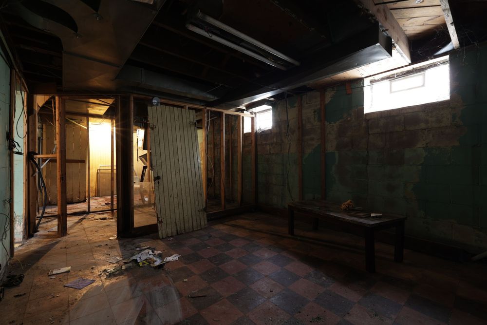 Abandoned basement interior with peeling walls, checkered floor, and dim natural light from small windows. Detroit Michigan
