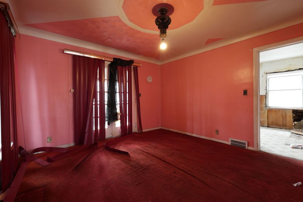 Empty room with pink walls, red carpet, tray ceiling, and dark curtains near a window. ceiling damage Detroit Michigan
