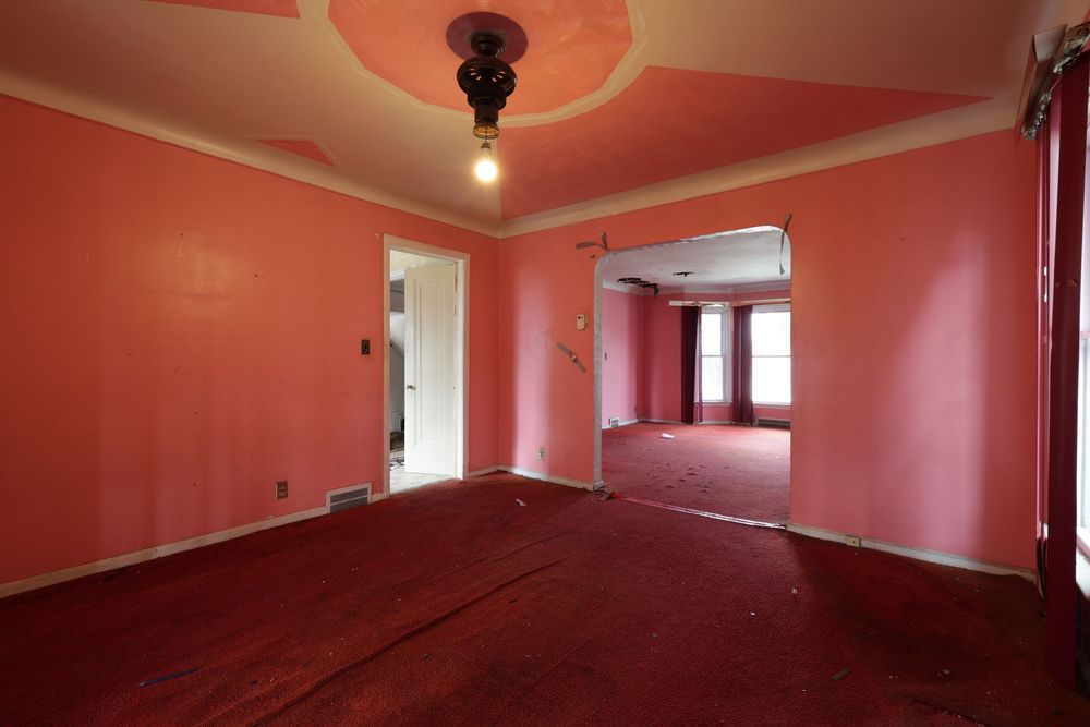 Pink-walled empty room with red hardwood floors, tray ceiling, and doorway to adjacent room. Detroit Michigan