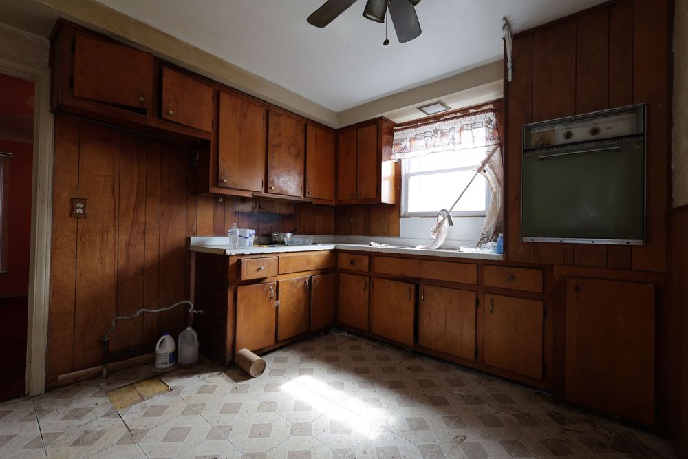 Dated kitchen with dark wood cabinets, vintage linoleum flooring, wall oven, and a window above the sink.