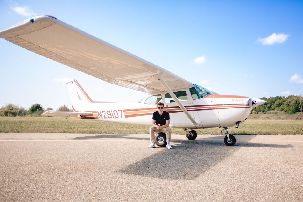 High school senior guy posing beside airplane during aviation themed senior photo session in Michigan by Brighton portrait photographer