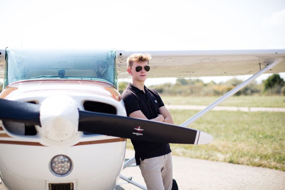 High school senior guy posing beside airplane during aviation themed senior photo session in Michigan by Brighton, MI portrait photographer
