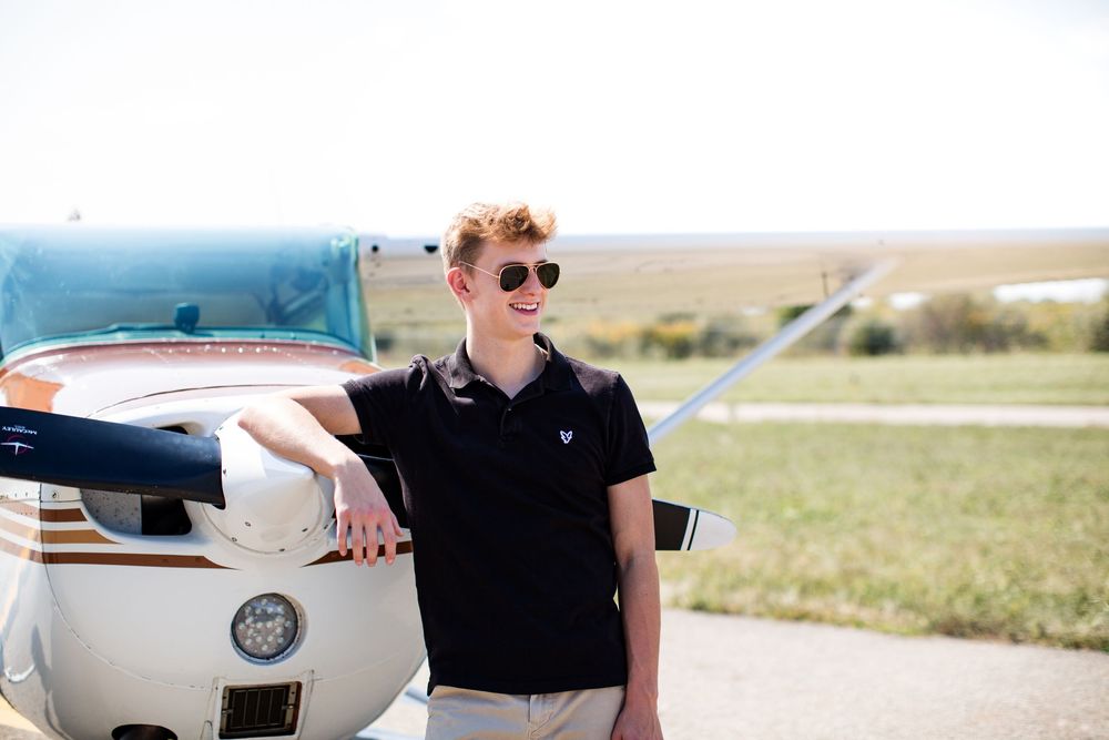 High school senior guy posing beside airplane during aviation themed senior portrait session in Michigan by South Lyon, MI photographer