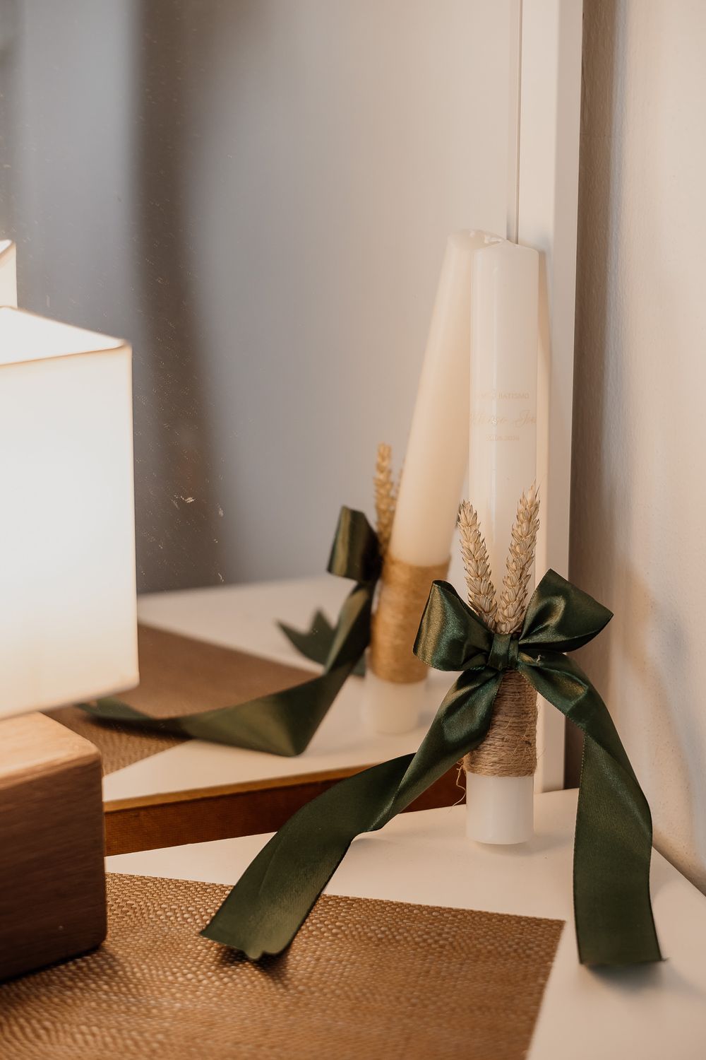 Elegant wedding candles wrapped in twine with dried wheat and dark green satin bows on a white surface.