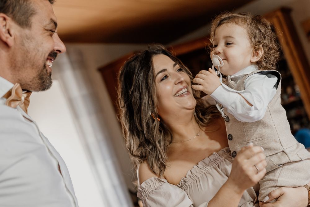 A joyful family moment with parents laughing and holding their adorable baby boy dressed in a smart outfit.