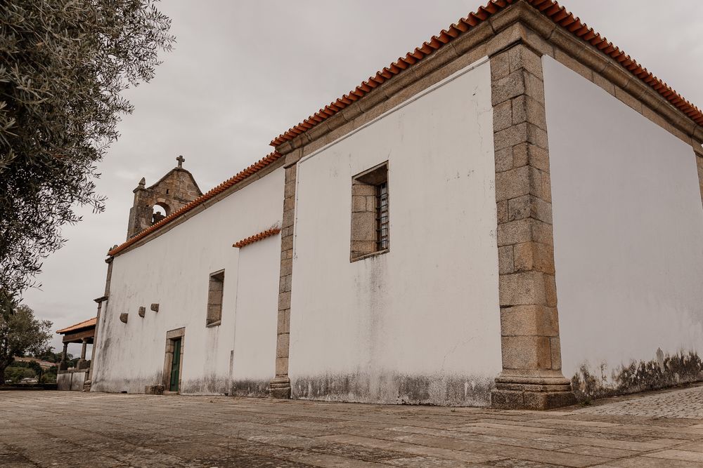 White historic church with stone pillar accents and red tile roof under overcast sky in Portugal.