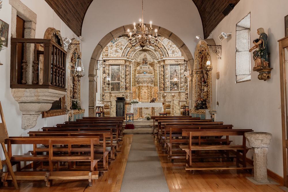 Interior of a historic Portuguese church with wooden pews, ornate gilded altar, and chandelier.